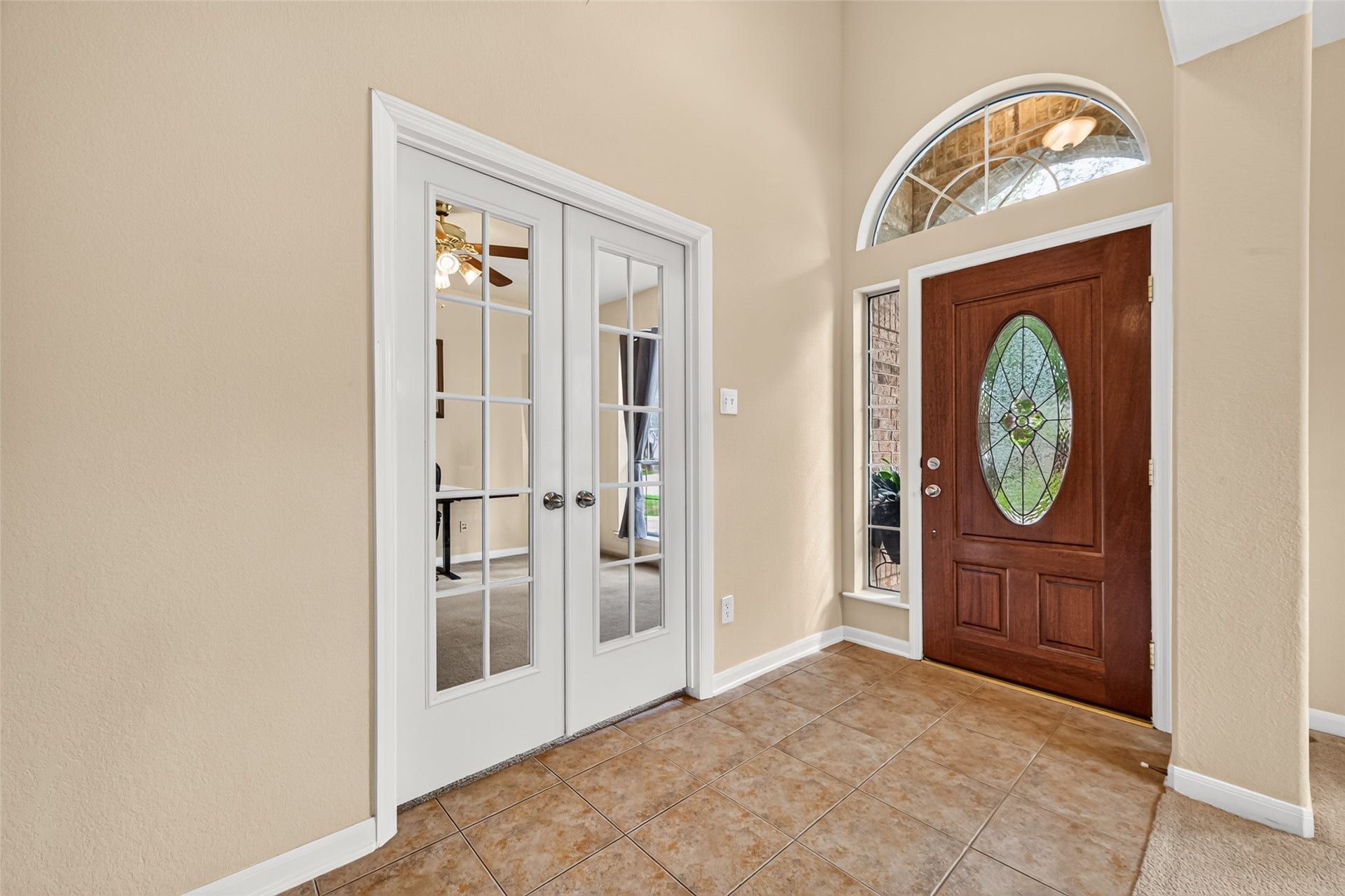 Bright, inviting entryway featuring a decorative glass front door, arched transom window, and French doors leading to the private home office.
