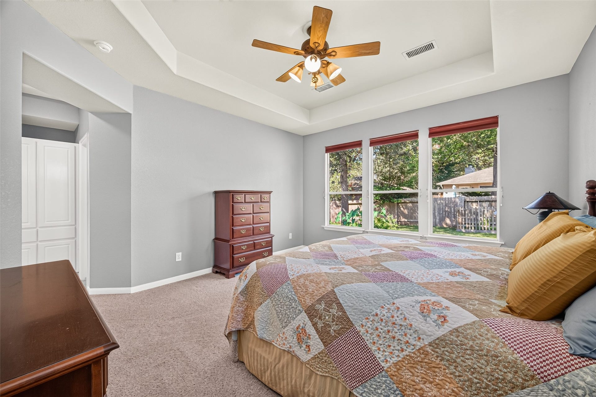 Another view of the primary bedroom highlighting the tray ceiling, generous floor space, and large windows with peaceful backyard views.
