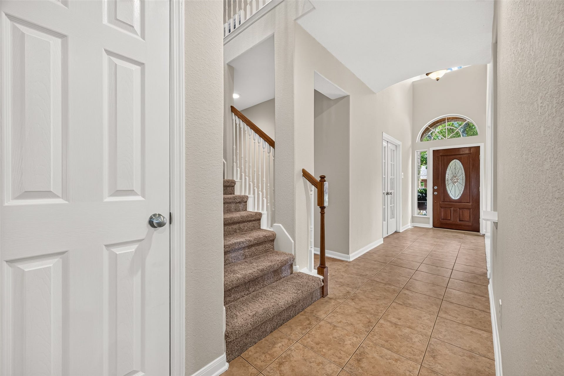 Another view of the spacious foyer showcasing the staircase with wood railing, tile flooring, and impressive two-story ceiling.