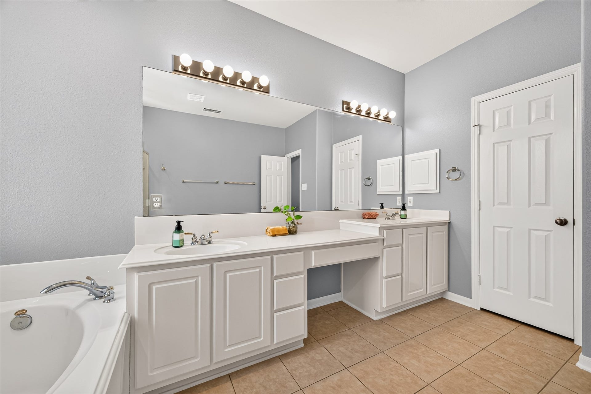 Primary bathroom offers dual vanities with generous counter space, ample cabinet storage, and a convenient seated makeup vanity area.
