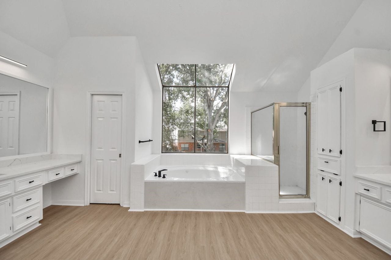 15047 Tramore Drive, Houston, TX 77083 The stunning primary bathroom features a bright, open design with dual vanities, extensive cabinetry, a large soaking tub, and a separate glass-enclosed shower.