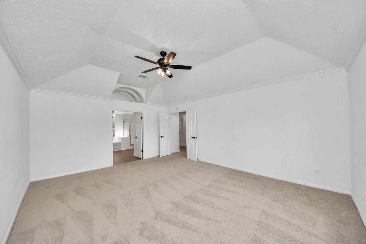 15047 Tramore Drive, Houston, TX 77083 Vaulted ceiling details, a ceiling fan, neutral carpeting, and the ensuite bathroom add to the rooms comfort and functionality.