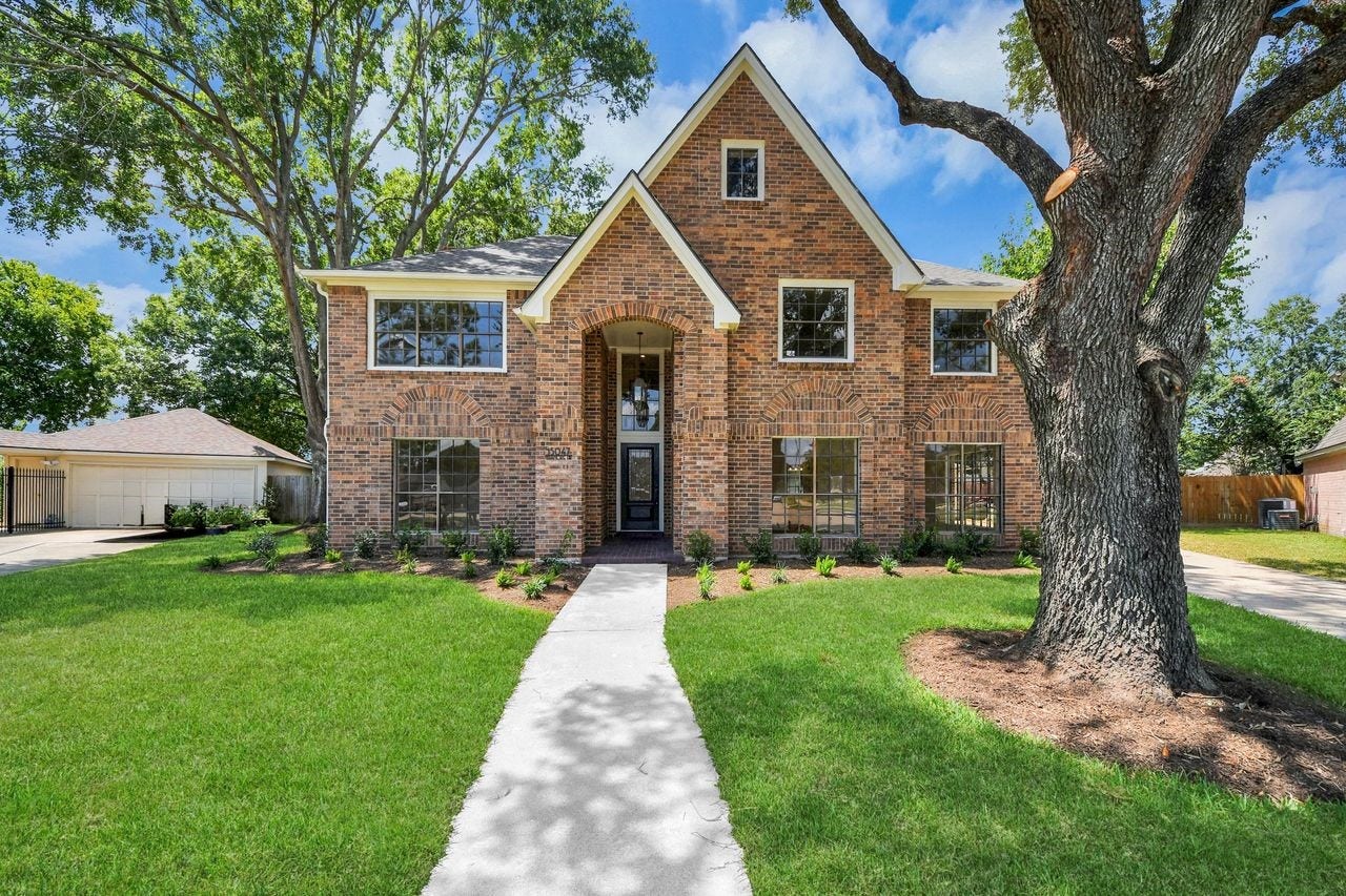 15047 Tramore Drive, Houston, TX 77083 A grand first impression begins beneath a canopy of mature trees. The classic brick exterior, timeless gables, lush lawn, and inviting walkway give this home a stately presence while keeping the curb appeal warm and welcoming.