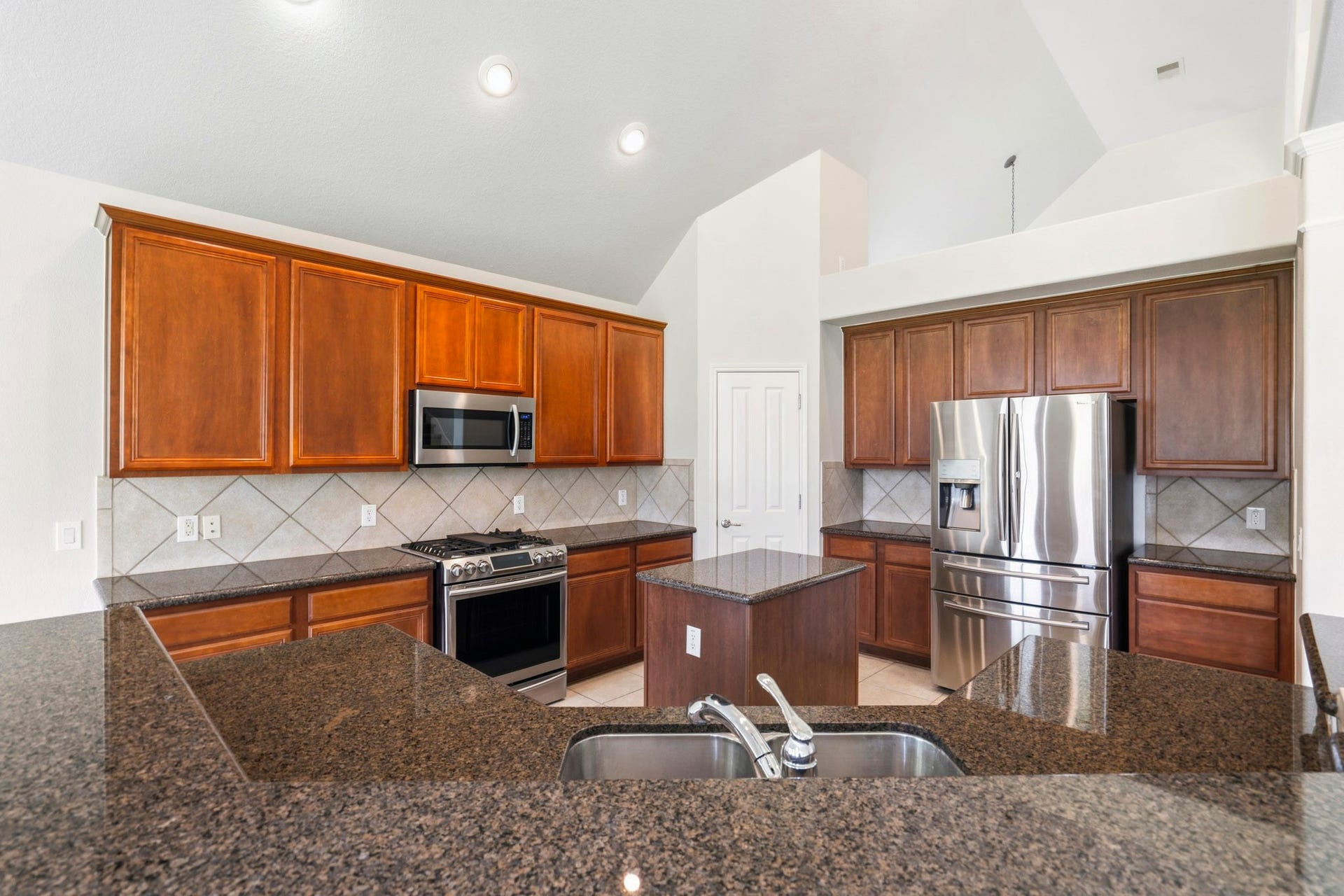 5515 Granite Meadow Drive, Katy, TX 77494 Chef-inspired kitchen featuring gleaming granite countertops, stainless steel appliances, a walk-in pantry, a five-burner gas cooktop with grill, center island, and included refrigerator.