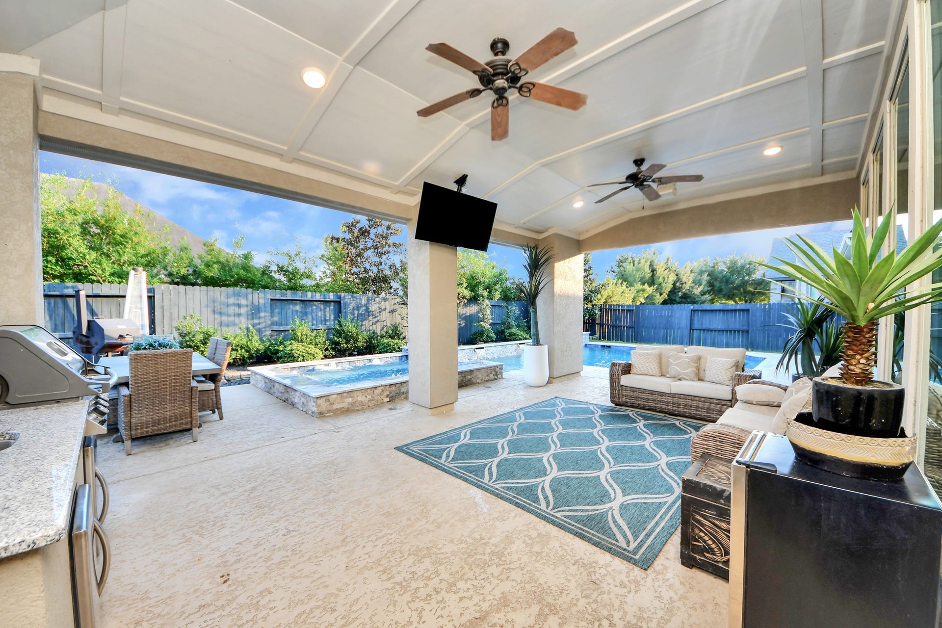 12821 N Palomino Lake Circle, Cypress, TX 77429 Expansive covered outdoor patio featuring stamped concrete, built-in speakers, two ceiling fans, mounted TV, and a fully equipped outdoor kitchen. Overlooking the oversized pool and spa, this private backyard oasis offers outdoor dining, mature landscaping, and exceptional privacy.