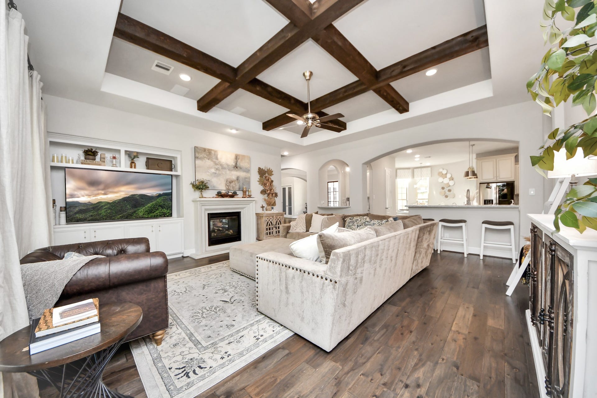12821 N Palomino Lake Circle, Cypress, TX 77429 Spacious family room featuring a coffered-style ceiling accented by exposed wood beams, elegant arched openings, built-in surround sound speakers, and a stunning double-sided fireplace.