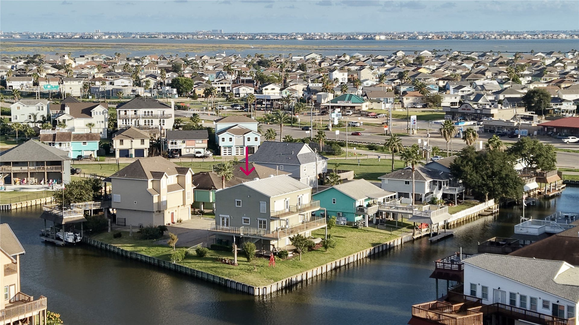 7 S Skimmer Street, La Marque, TX 77568 Aerial view of the home on its point lot, with water on two sides and a bulkhead wrapping the property. Across Highway 6 you can see Bayou Vista, and Tiki Island sits on the horizon, a clear picture of how connected this corner of the coast is.