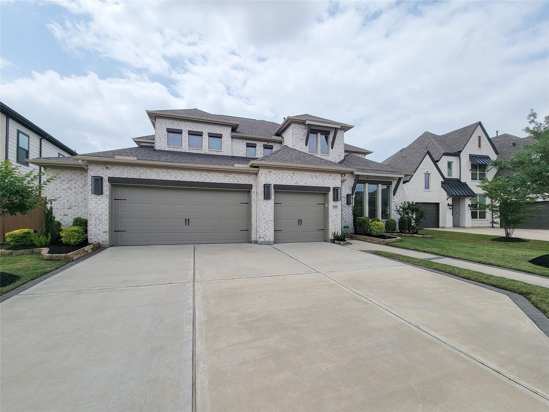 This is a modern two-story brick home with a three-car garage and well-maintained landscaping. The facade features large windows and a spacious driveway in a suburban neighborhood.