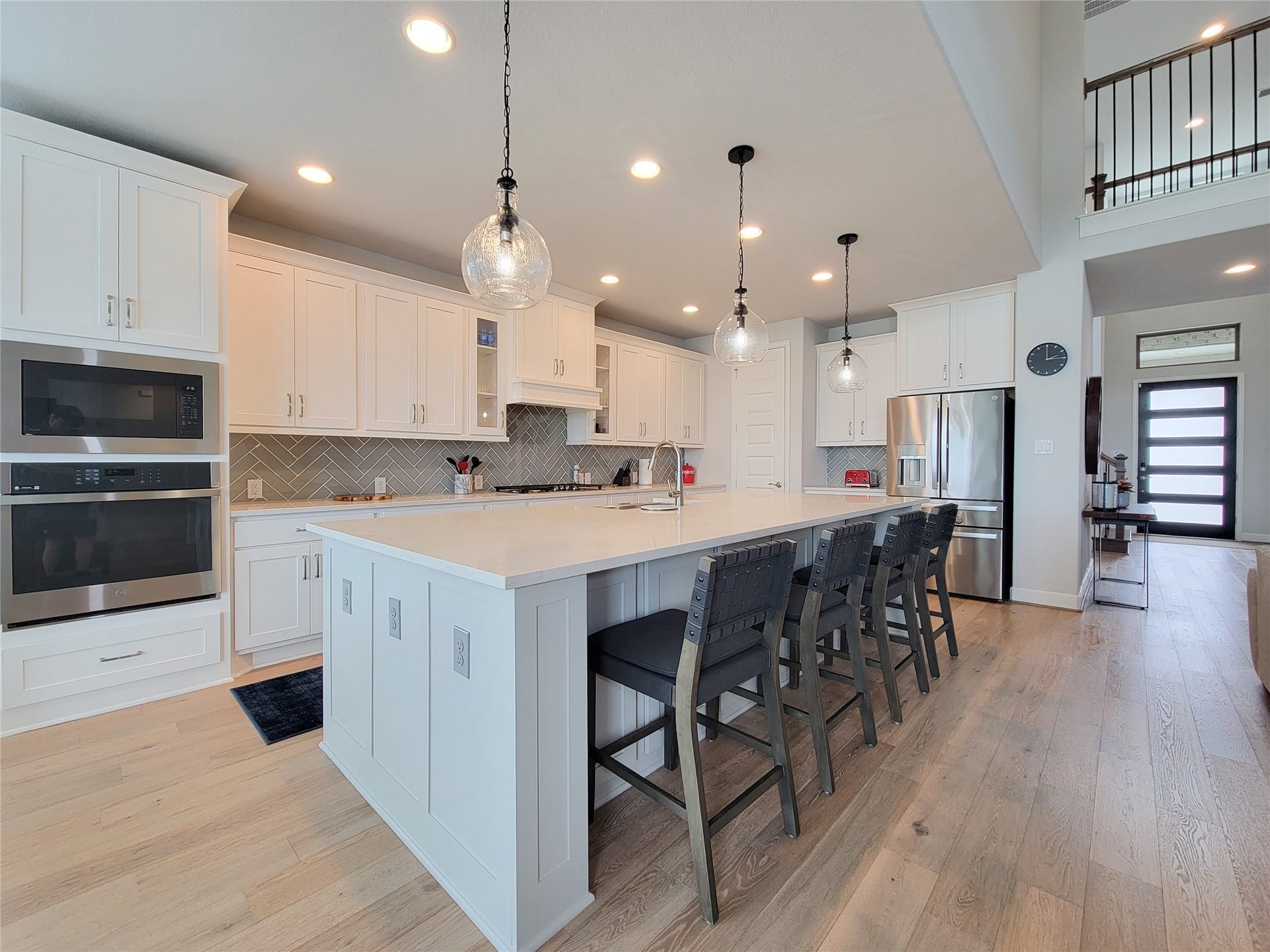This modern kitchen features sleek white cabinetry, a spacious island with seating, stainless steel appliances, and stylish pendant lighting, creating a bright and inviting space.