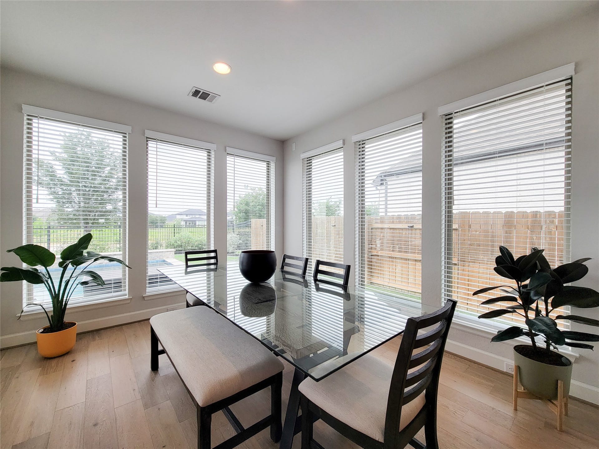 Bright dining area with large windows and a view of the backyard. Features a glass-top table, modern chairs, and wood flooring, creating a welcoming and airy atmosphere.