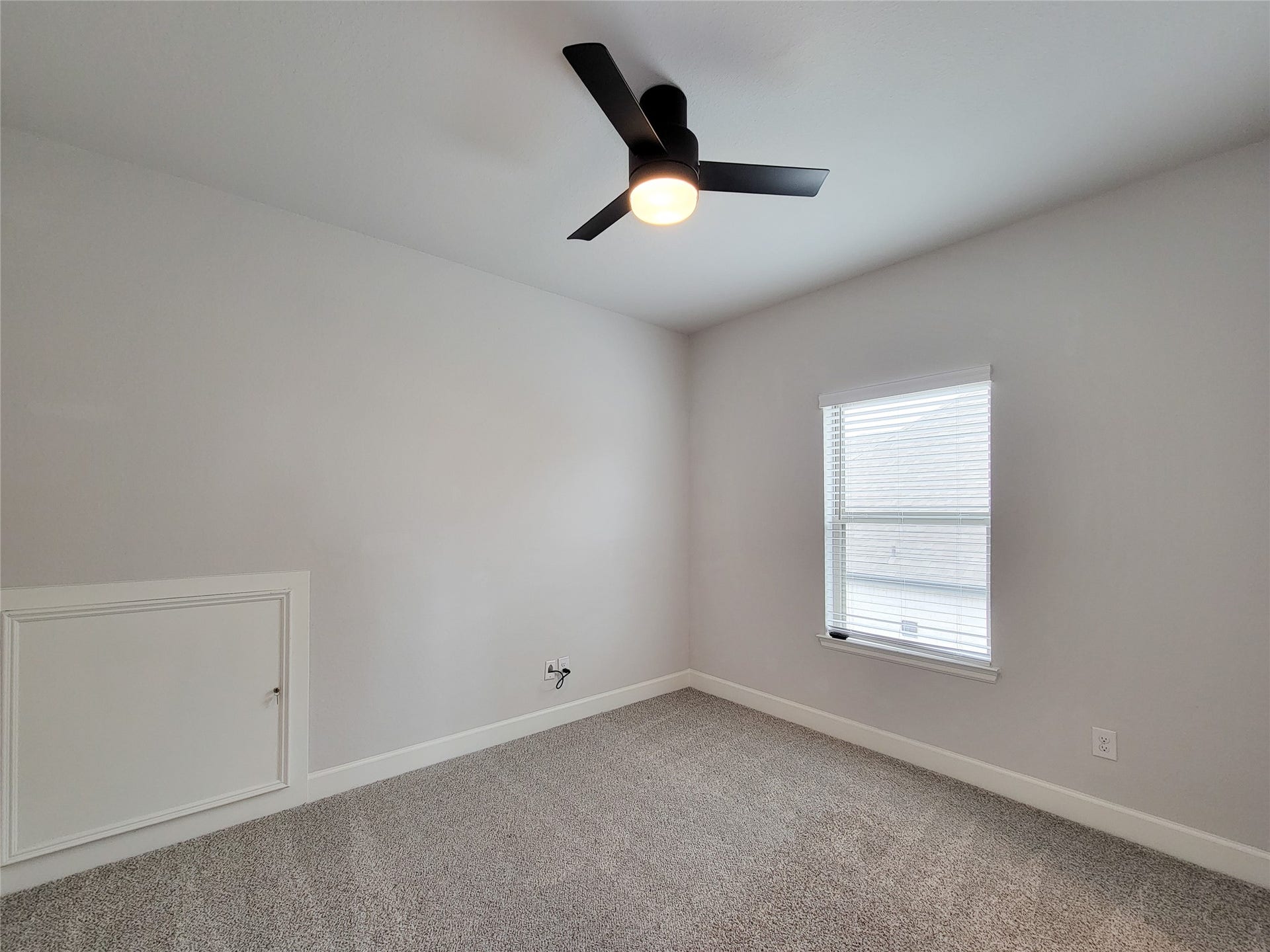 This Bedroom shows a bright, small room with neutral-color walls and carpet. It features a modern ceiling fan and a window with blinds, providing natural light.