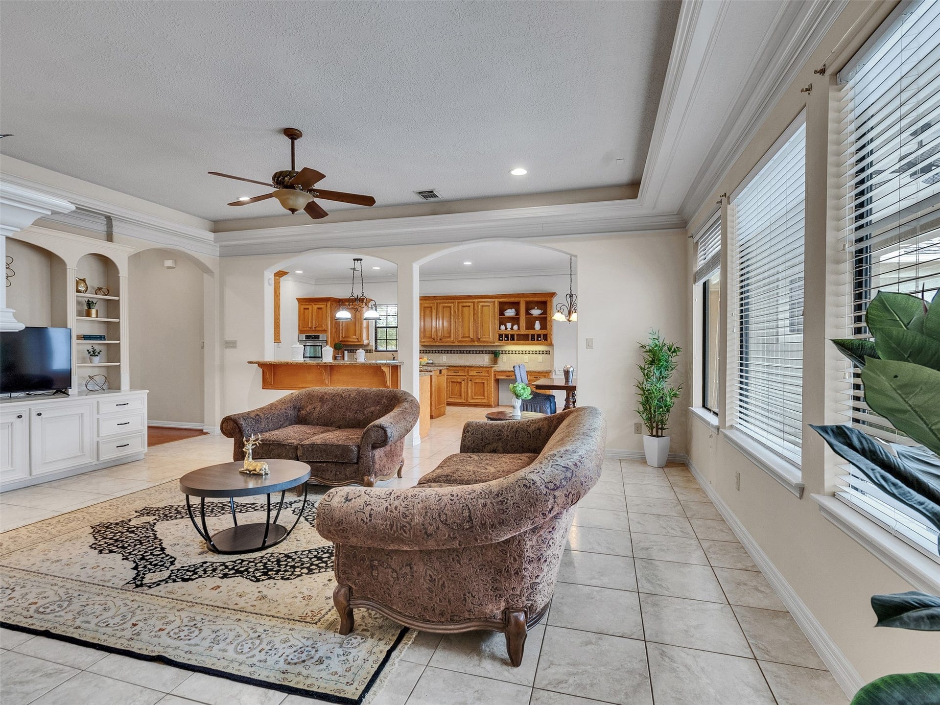 6914 Sandwedge Point Court, Spring, TX 77389 This spacious living area features large windows for natural light, tiled flooring, and a cozy seating arrangement. It flows into an open kitchen with wooden cabinetry and a breakfast bar, offering a welcoming atmosphere for family gatherings.