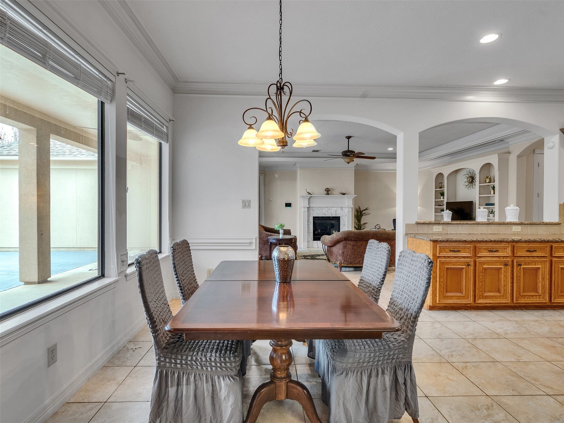 6914 Sandwedge Point Court, Spring, TX 77389 This spacious, well-lit dining area features large windows with views of the patio. It opens into a cozy living room with a fireplace and built-in shelving. The adjacent kitchen has a granite countertop island and wooden cabinetry, creating a warm, inviting atmosphere.