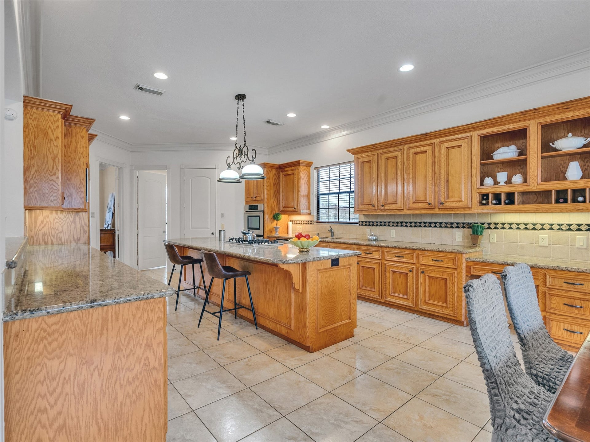 6914 Sandwedge Point Court, Spring, TX 77389 This spacious kitchen features warm wood cabinetry, granite countertops, and a large island with a gas cooktop. It's well-lit with recessed lighting and a stylish pendant fixture, complemented by tile flooring and a cozy seating area.