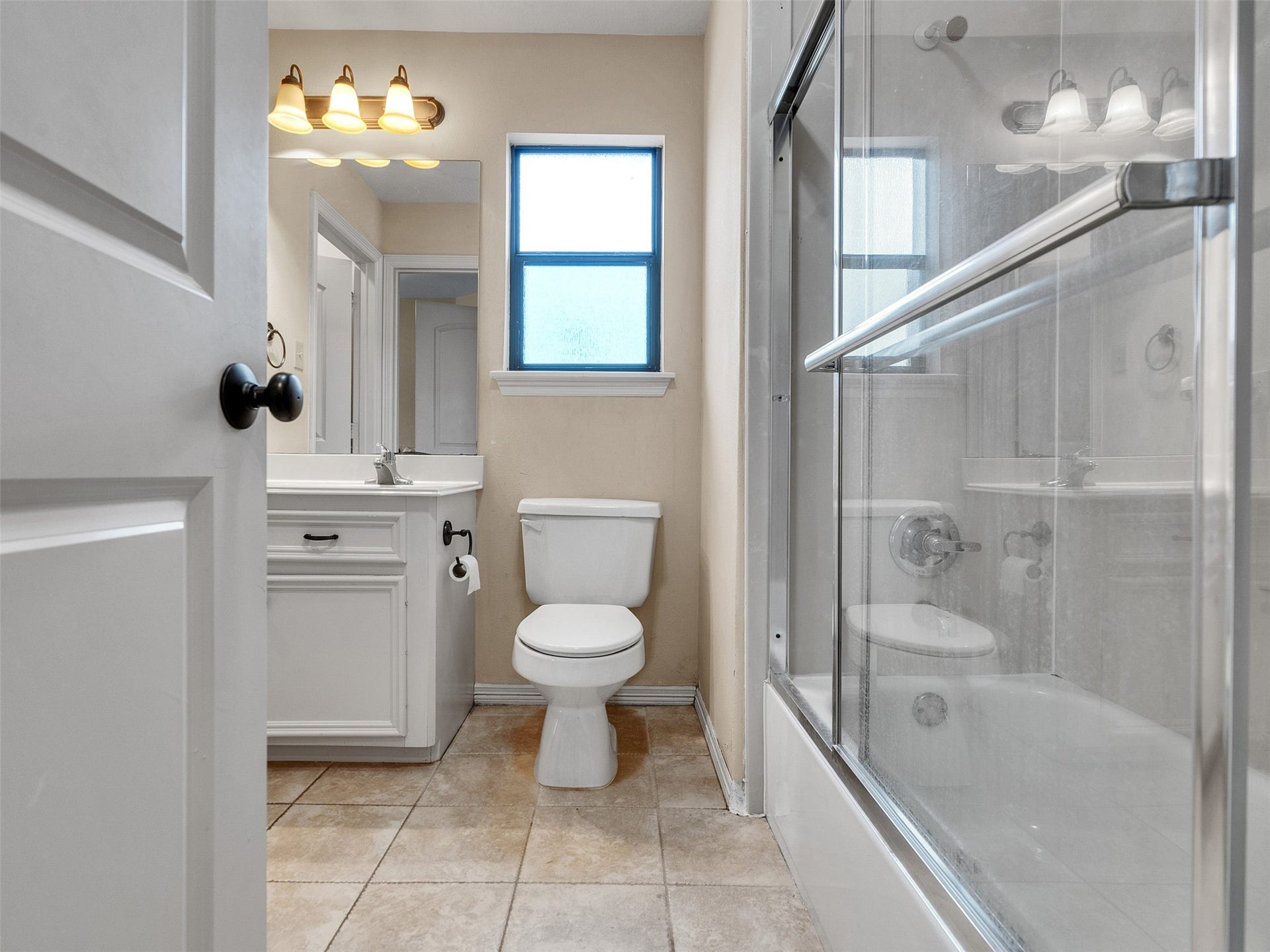 6914 Sandwedge Point Court, Spring, TX 77389 This bathroom features a clean, modern design with a tiled floor, a glass-enclosed bathtub, a white vanity, and a window for natural light.