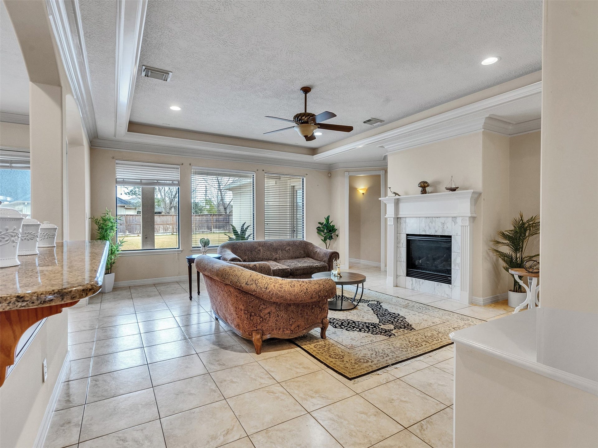 6914 Sandwedge Point Court, Spring, TX 77389 This elegant living room features a cozy fireplace, large windows with ample natural light, and a ceiling fan. The space is adorned with a plush sofa set and tasteful decor, offering a welcoming and comfortable atmosphere.