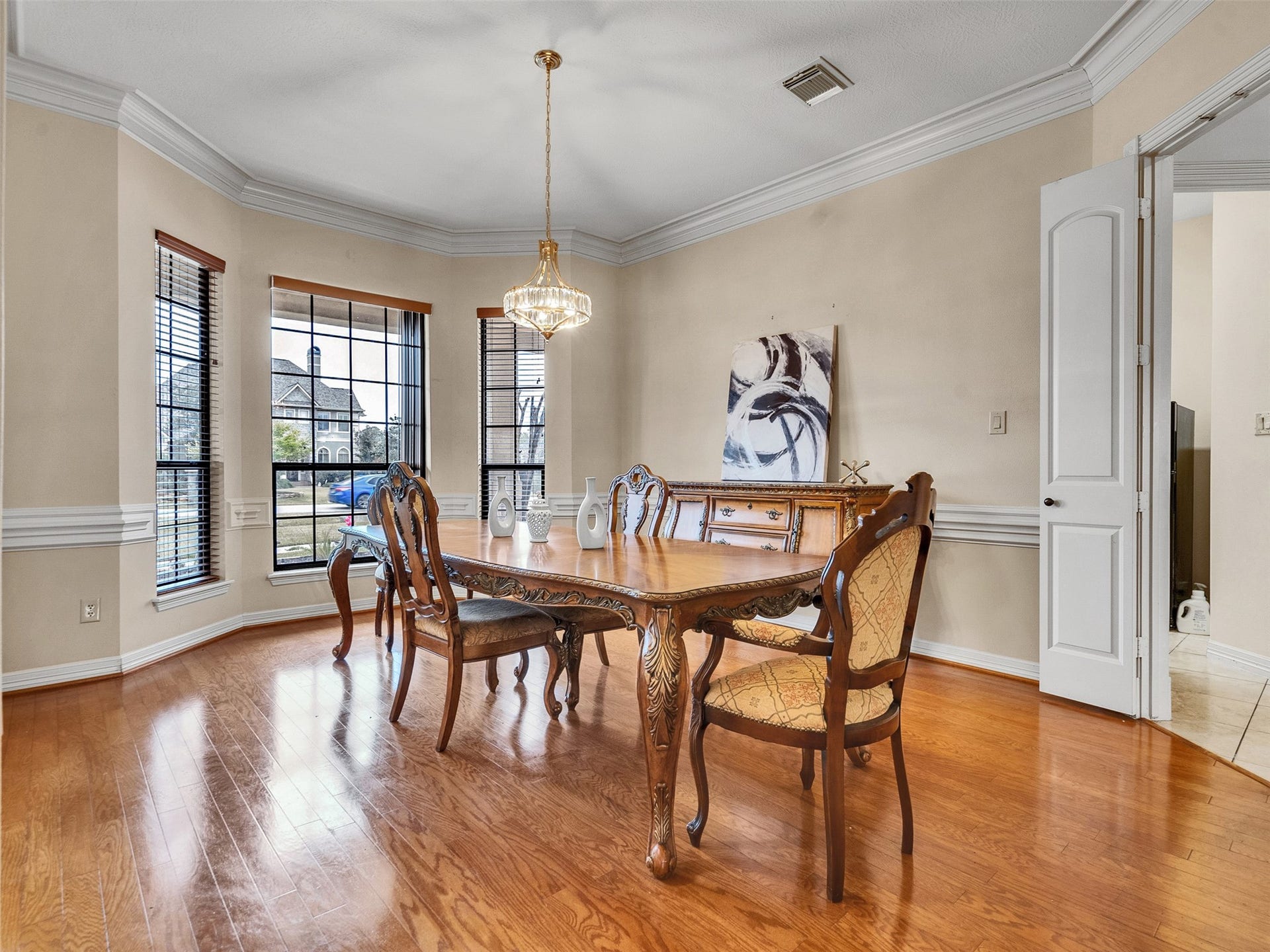 6914 Sandwedge Point Court, Spring, TX 77389 This elegant dining room features hardwood floors, a large window with ample natural light, a classic wooden dining set, and a stylish chandelier. The space is complemented by crown molding and neutral walls, creating a warm and inviting atmosphere.