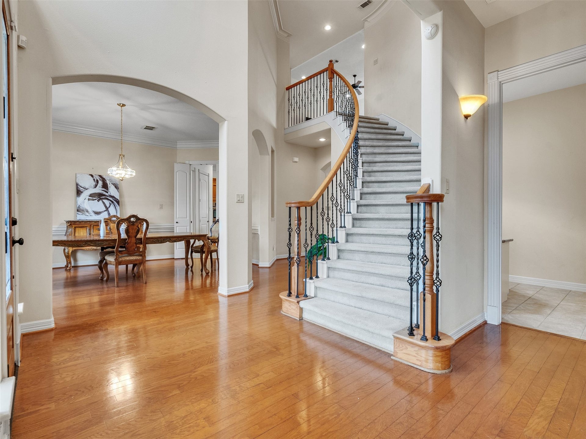 6914 Sandwedge Point Court, Spring, TX 77389 This elegant home features a grand curved staircase with iron balusters and a bright, open layout. The entryway showcases hardwood floors leading to a formal dining area, highlighted by an arched doorway and a stylish chandelier.