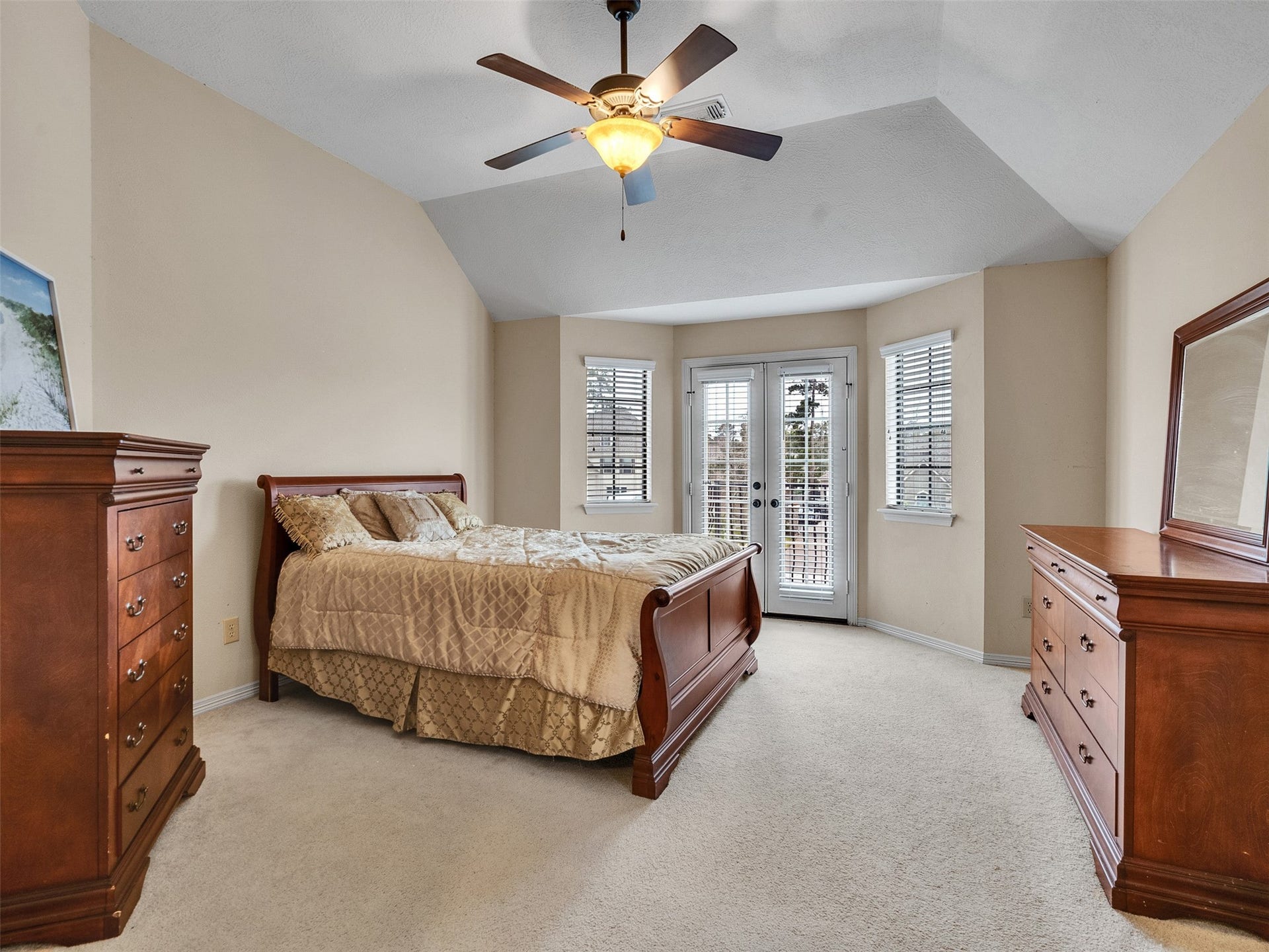 6914 Sandwedge Point Court, Spring, TX 77389 Spacious bedroom with a vaulted ceiling and neutral tones. Features a ceiling fan and natural light from large windows and French doors. Includes elegant wooden furniture and plush carpeting for a cozy feel.