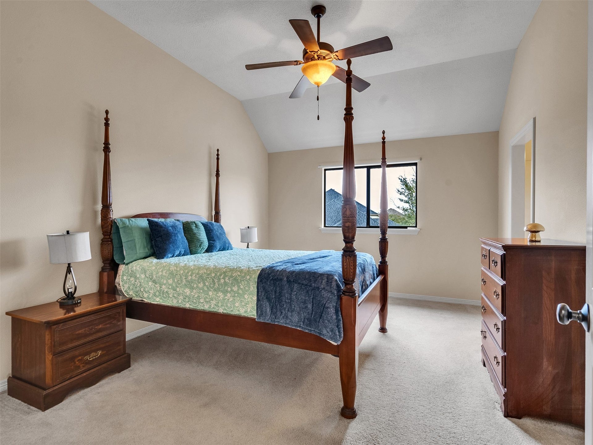 6914 Sandwedge Point Court, Spring, TX 77389 This bedroom features a high ceiling with a ceiling fan, a large window providing natural light, and is furnished with a four-poster bed, nightstand, and dresser, all in rich wood tones. The neutral walls and carpet add to the spacious and inviting atmosphere.