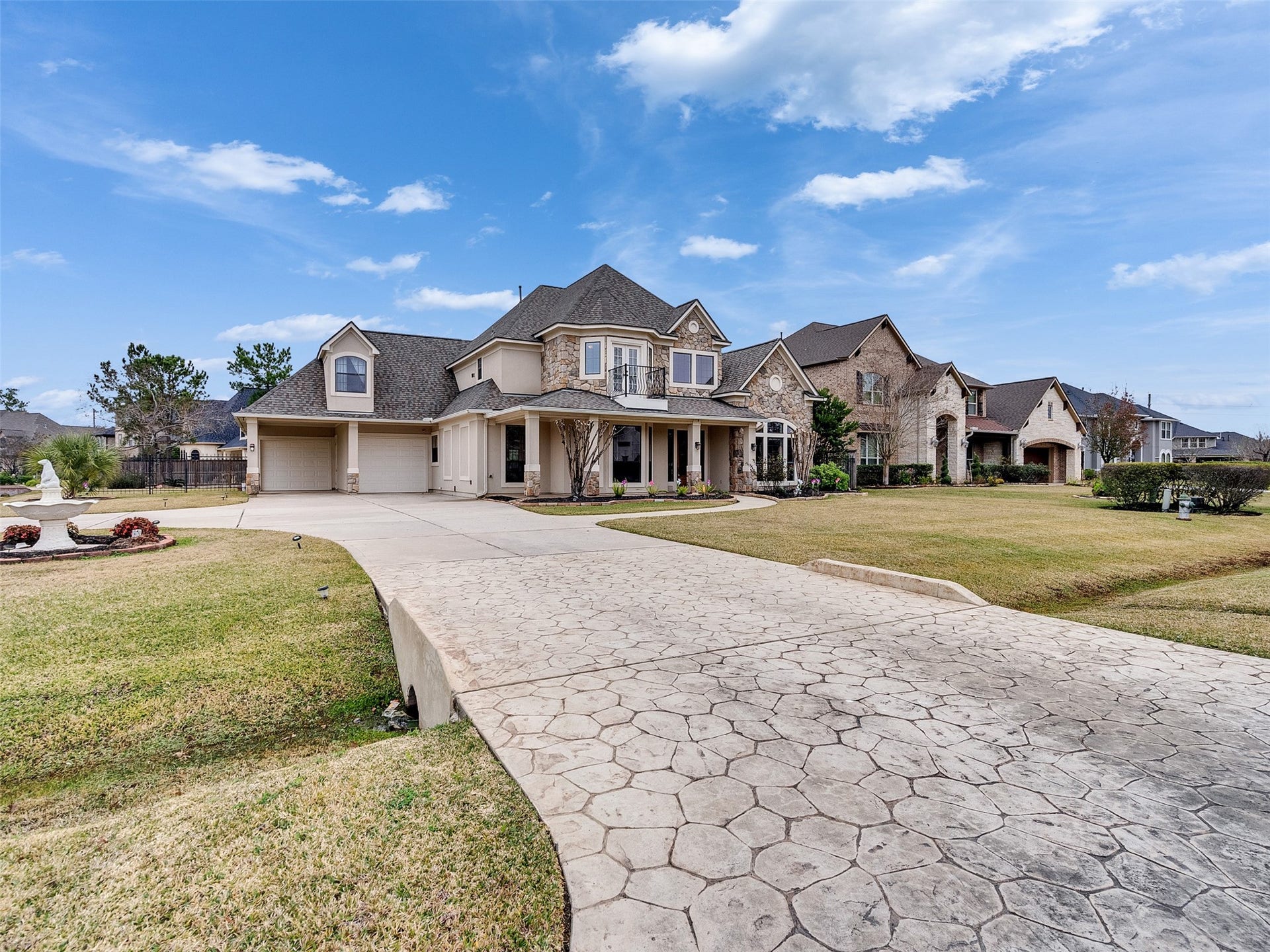 6914 Sandwedge Point Court, Spring, TX 77389 Elegant two-story home with a stone facade and a spacious three-car garage. The property features a large, patterned concrete driveway and well-maintained landscaping, set in a picturesque neighborhood.