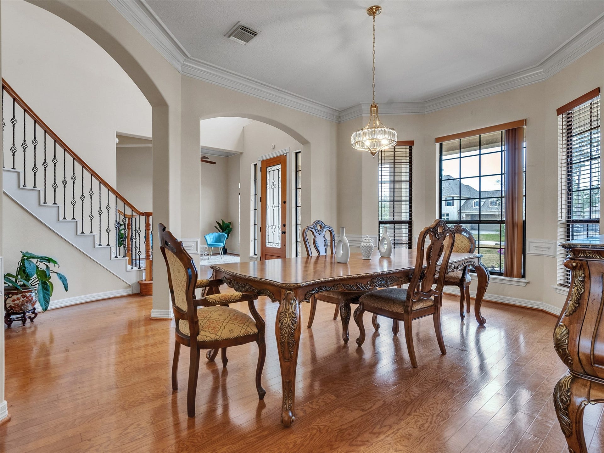 6914 Sandwedge Point Court, Spring, TX 77389 This elegant dining area features hardwood floors, a classic chandelier, and large windows offering natural light. The room showcases ornate wood furniture and leads to a staircase with decorative iron railings, creating a sophisticated ambiance.