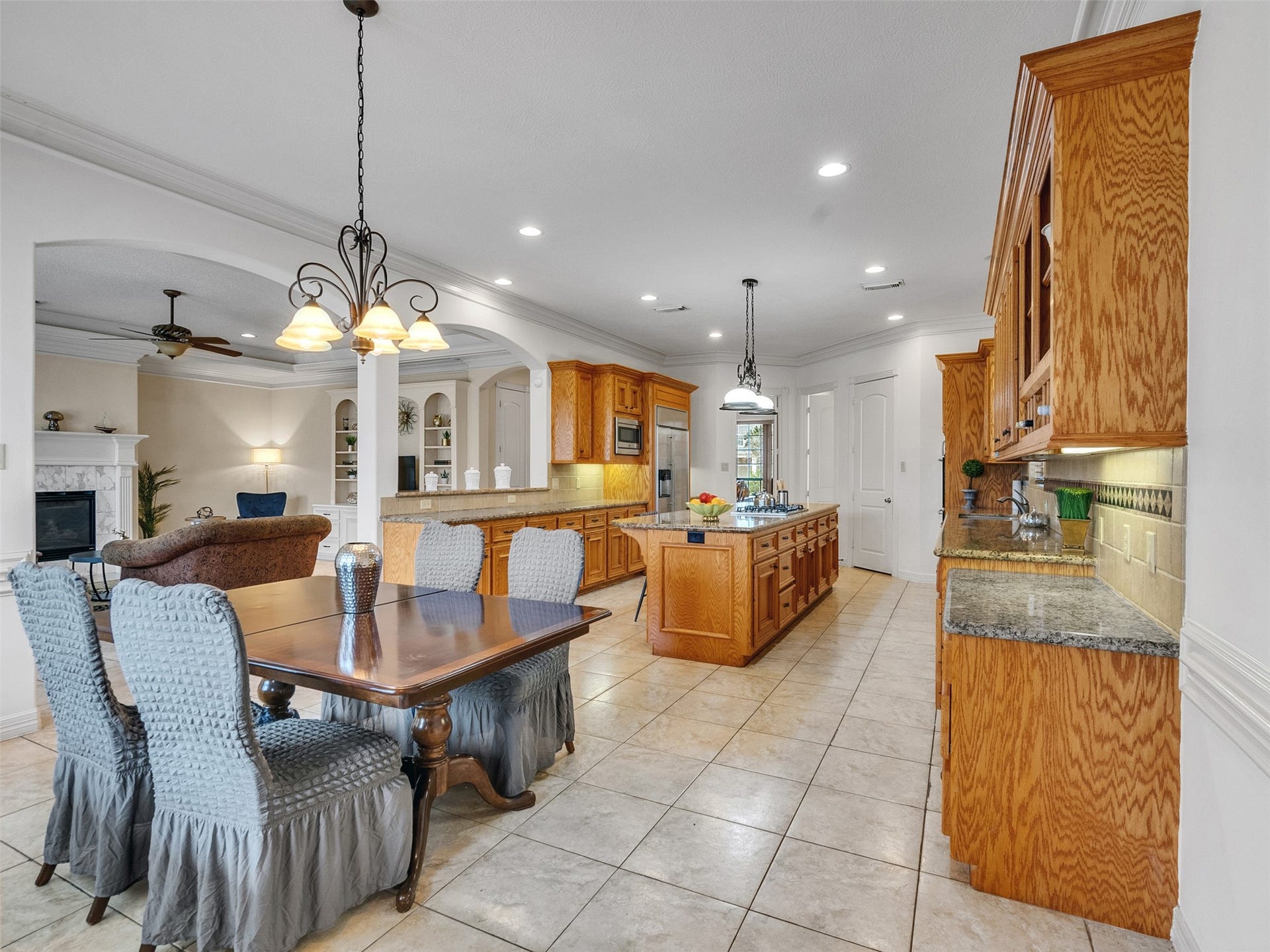 6914 Sandwedge Point Court, Spring, TX 77389 This spacious kitchen features warm wood cabinetry, a large island with granite countertops, and tile flooring. It's open to a cozy living area with a fireplace, ideal for entertaining.