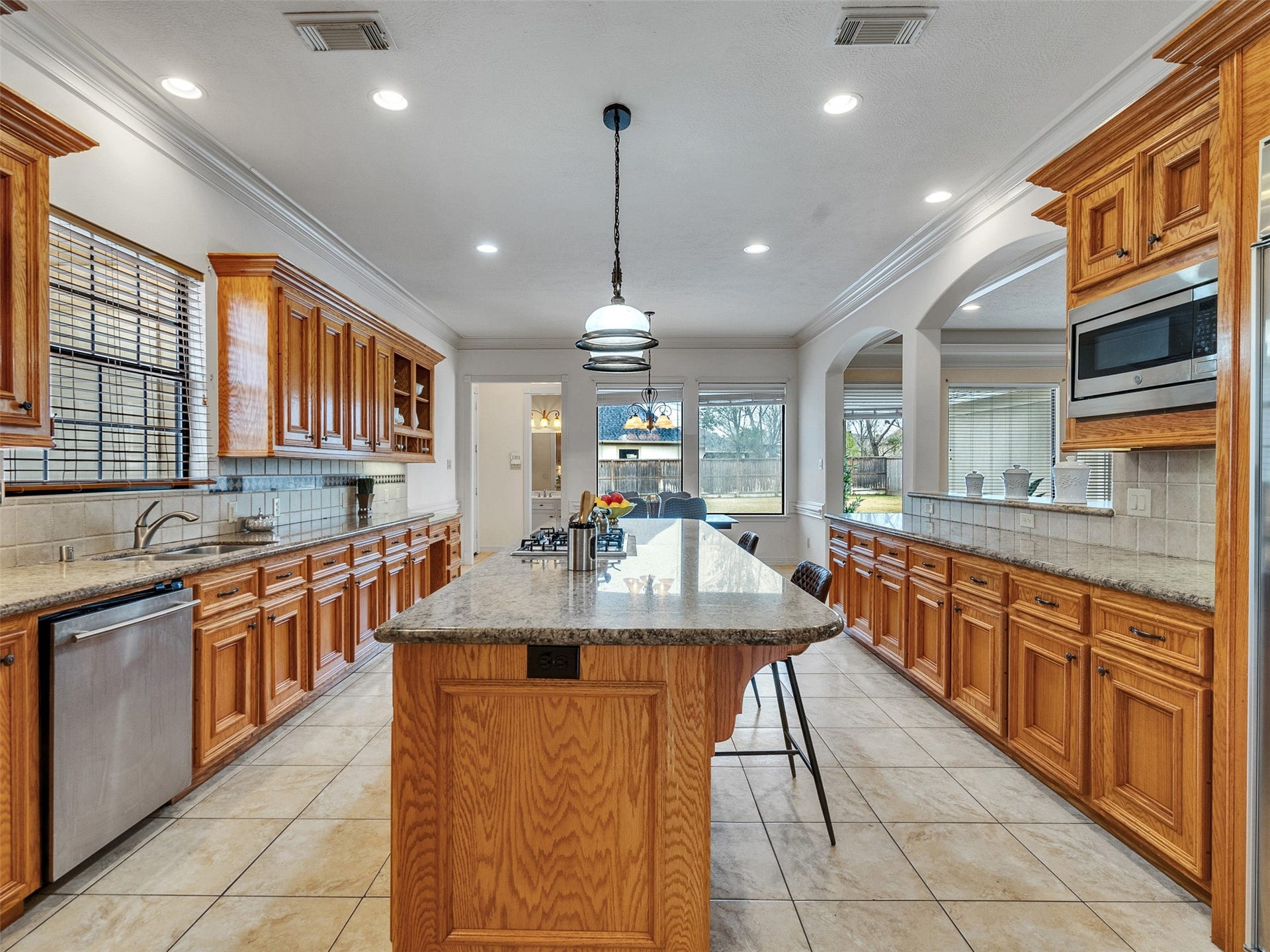 6914 Sandwedge Point Court, Spring, TX 77389 This spacious kitchen features warm wood cabinetry, granite countertops, and a large central island with seating. It offers ample storage and modern appliances, creating a welcoming space for cooking and entertaining. Large windows provide plenty of natural light and a view of the backyard.