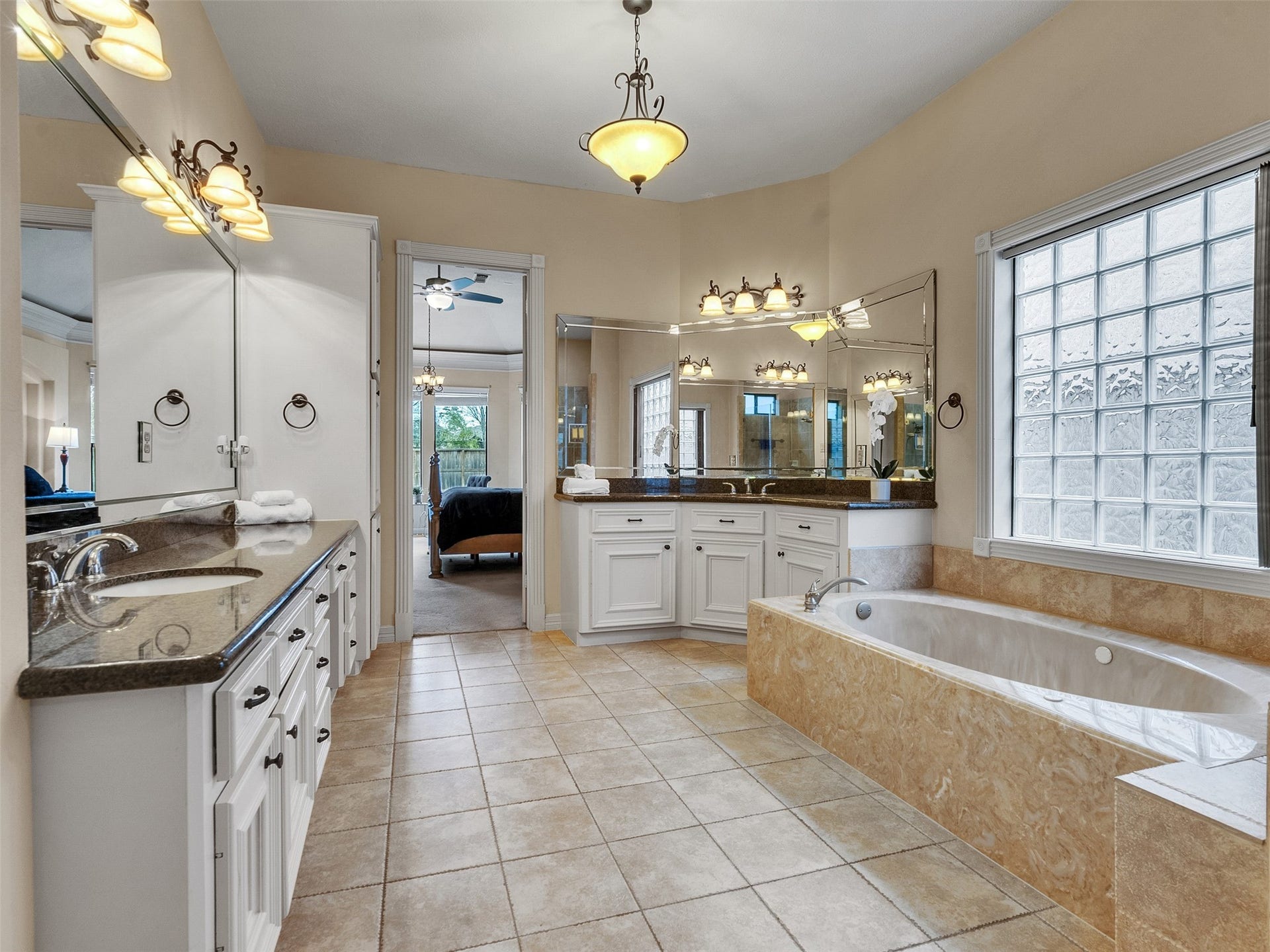 6914 Sandwedge Point Court, Spring, TX 77389 This spacious bathroom features a luxurious soaking tub, dual sinks with granite countertops, and ample lighting. It boasts large mirrors, elegant fixtures, and a frosted glass window for natural light and privacy.