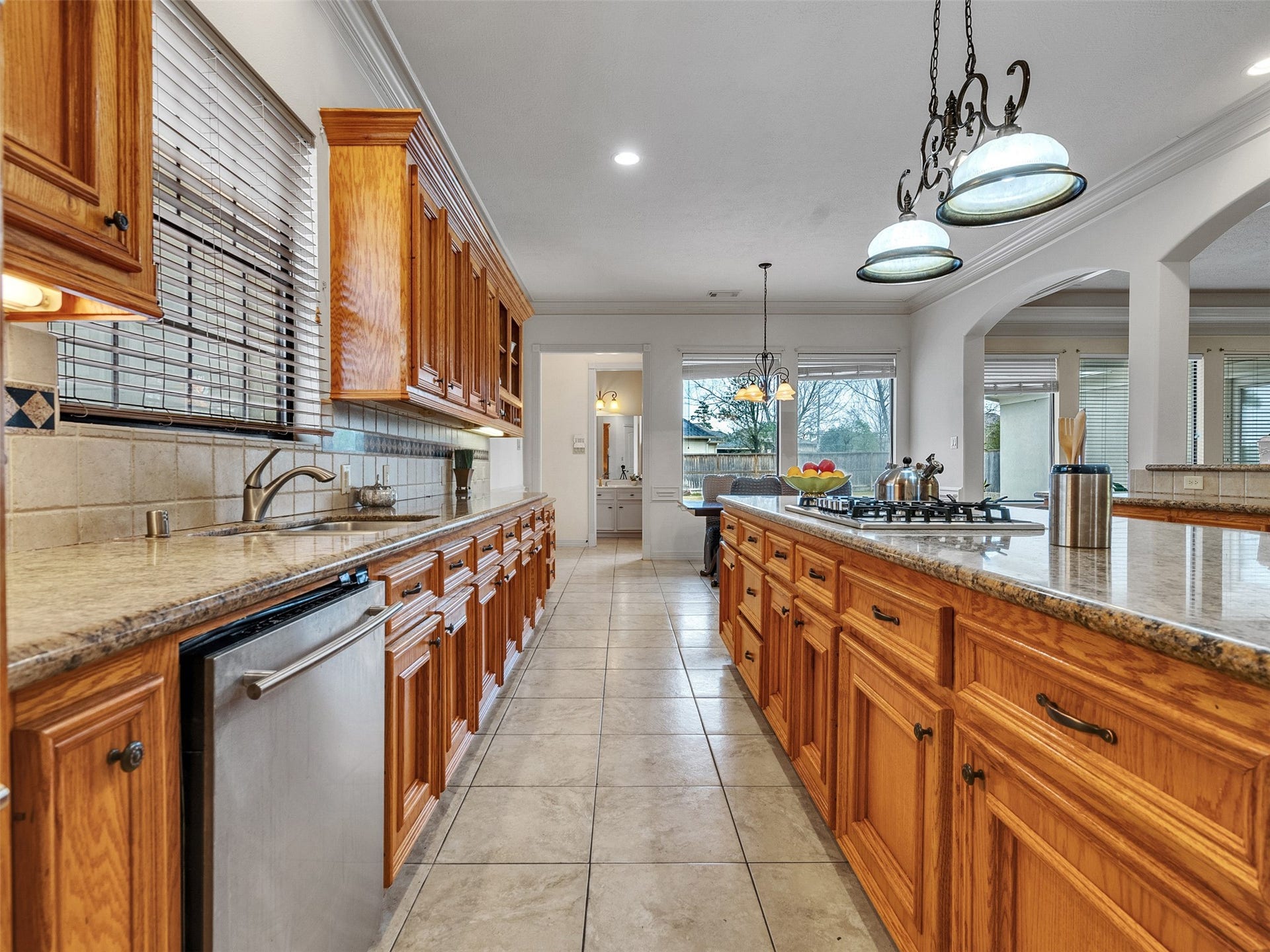 6914 Sandwedge Point Court, Spring, TX 77389 Spacious kitchen with ample natural light, featuring wooden cabinetry, granite countertops, and a central island with a built-in cooktop. The tiled floor and large windows enhance the open, inviting atmosphere.