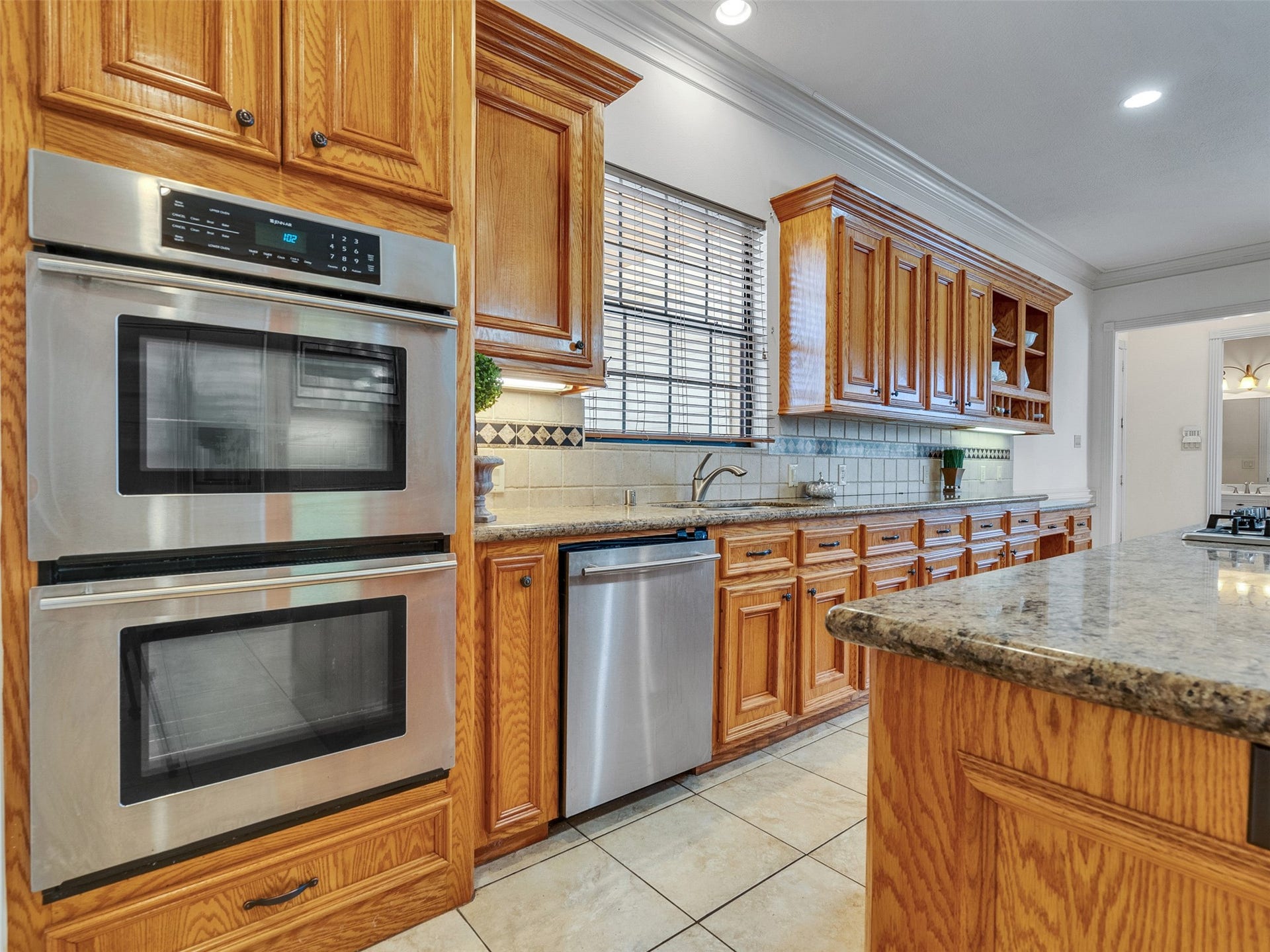 6914 Sandwedge Point Court, Spring, TX 77389 Spacious kitchen with warm wooden cabinetry, stainless steel double ovens, and granite countertops. Features a tile backsplash, under-cabinet lighting, and ample natural light from a large window above the sink.