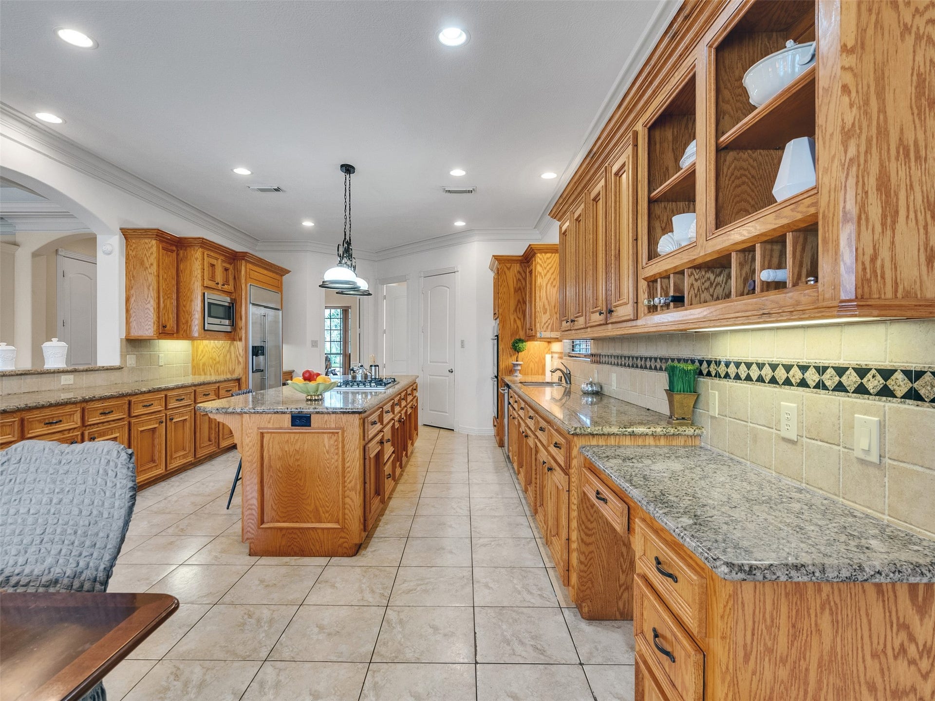 6914 Sandwedge Point Court, Spring, TX 77389 This photo showcases a spacious kitchen with ample wooden cabinetry, granite countertops, and a central island. The room features tiled flooring, recessed lighting, and modern appliances, offering a warm and functional cooking space.
