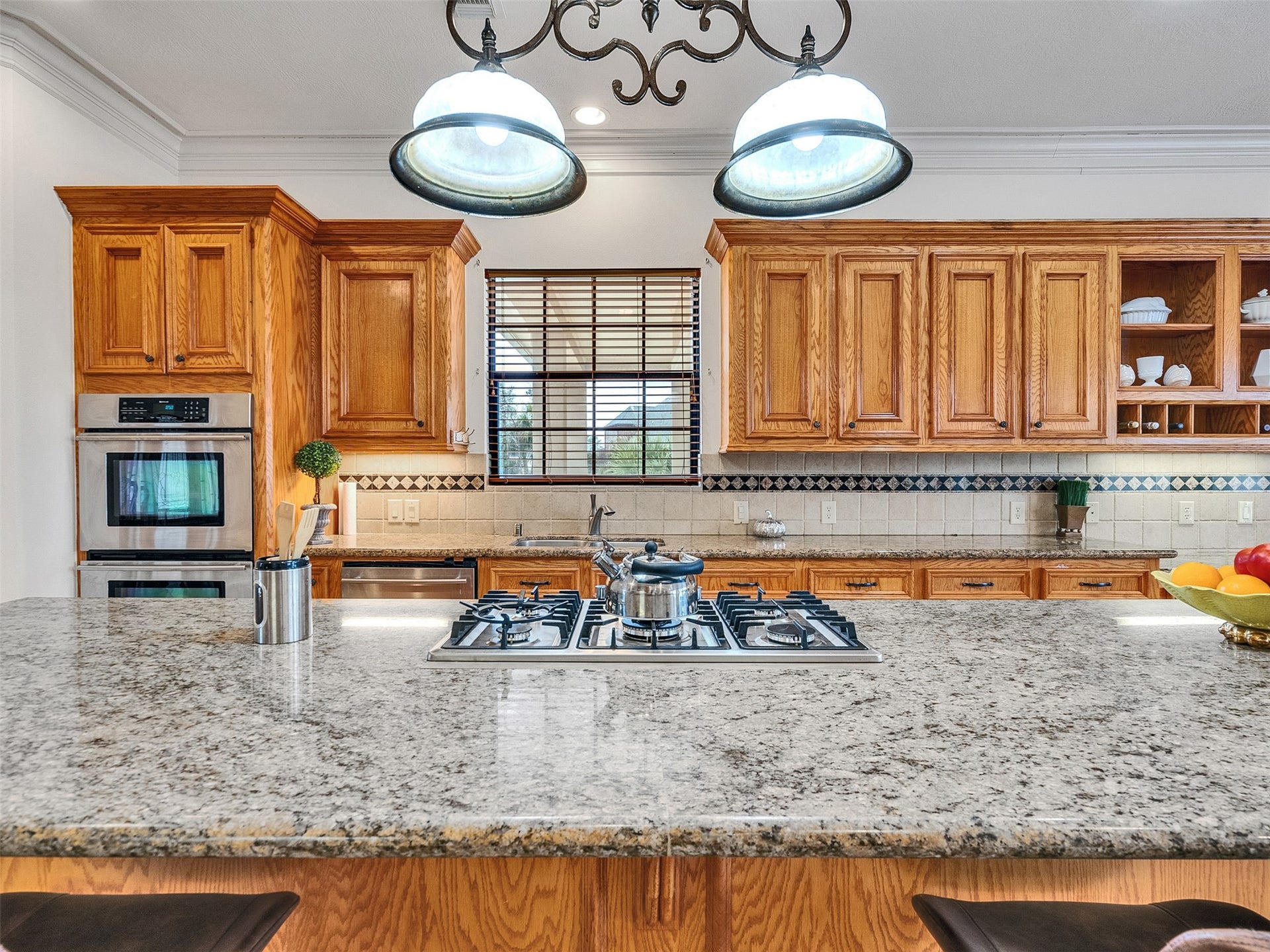 6914 Sandwedge Point Court, Spring, TX 77389 This spacious kitchen features granite countertops, a central island with a gas cooktop, and warm wood cabinetry. It includes double ovens, ample storage, and a classic tile backsplash, creating a welcoming and functional space.