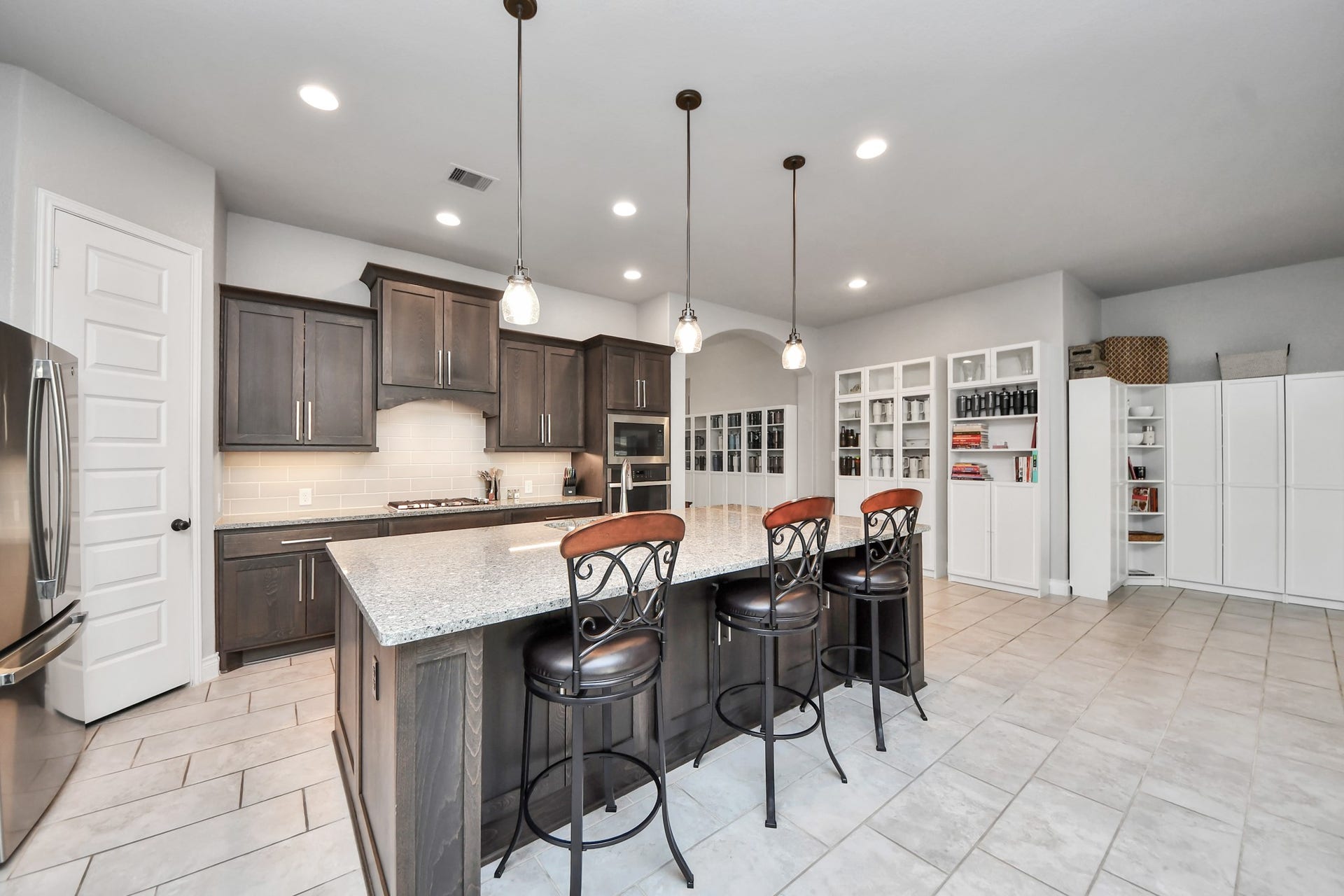 3211 Sweet Audrey Lane, Richmond, TX 77406 Rich stained cabinetry, tile backsplash, and a stacked wall oven and microwave round out this chef-ready kitchen.