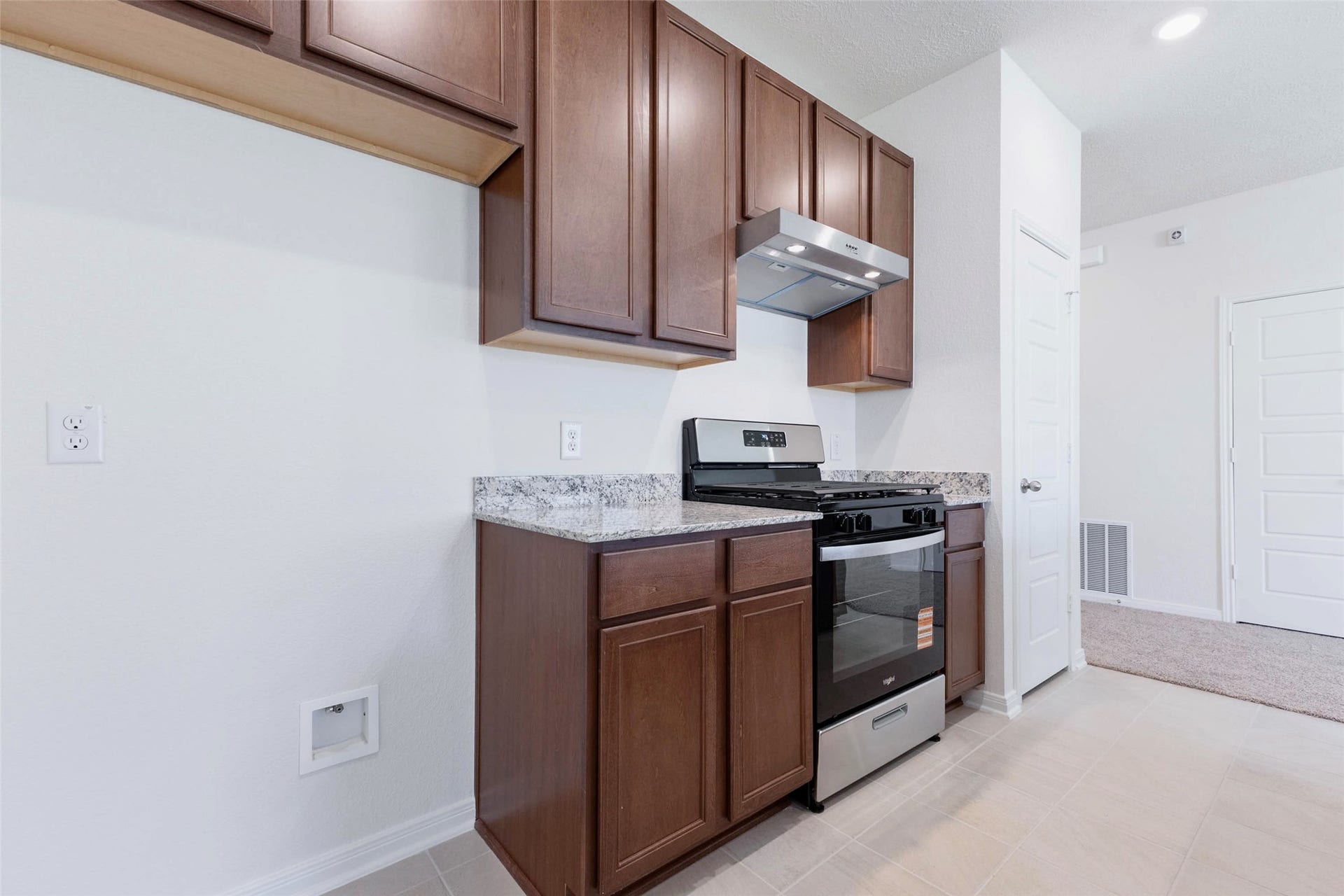 A new stainless steel gas range and vent hood sit between granite countertops and rich wood cabinetry.