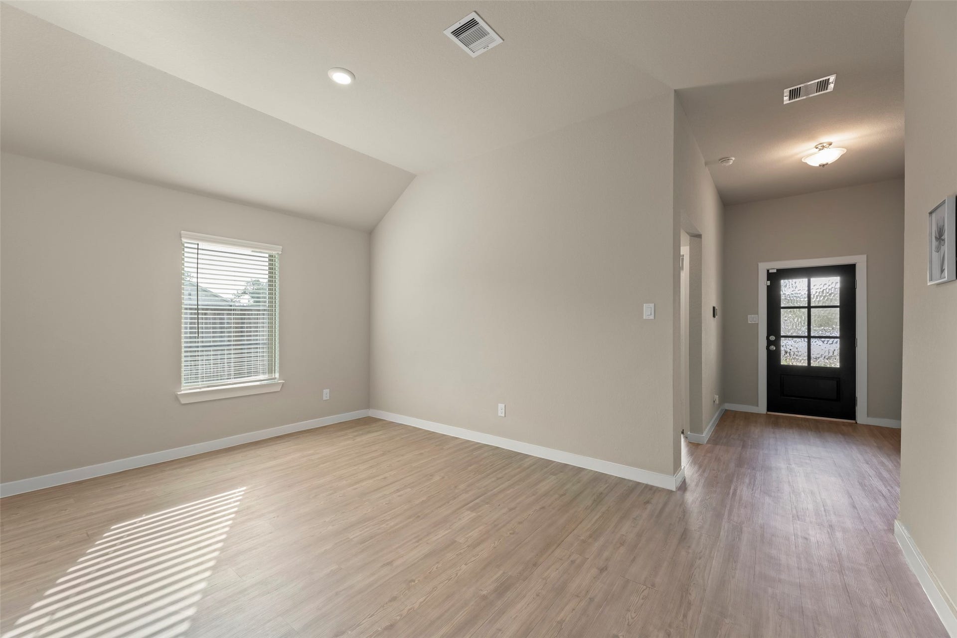 2610 Blue Abbot Drive, Fresno, TX 77545 Bright family room space with high ceilings, sleek laminate flooring, and a stylish black front door, perfect for a modern touch.