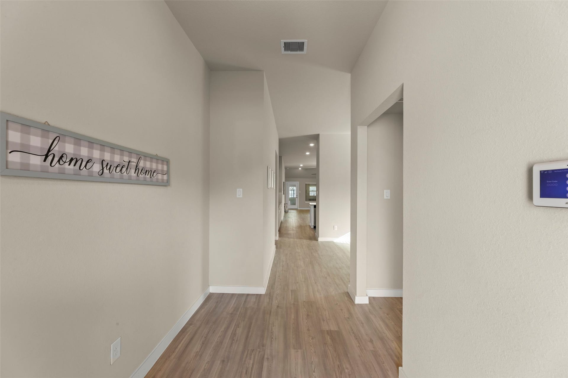 2610 Blue Abbot Drive, Fresno, TX 77545 Inviting hallway with warm wood floors and neutral walls, leading to an open living area, accented by a charming "home sweet home" sign.