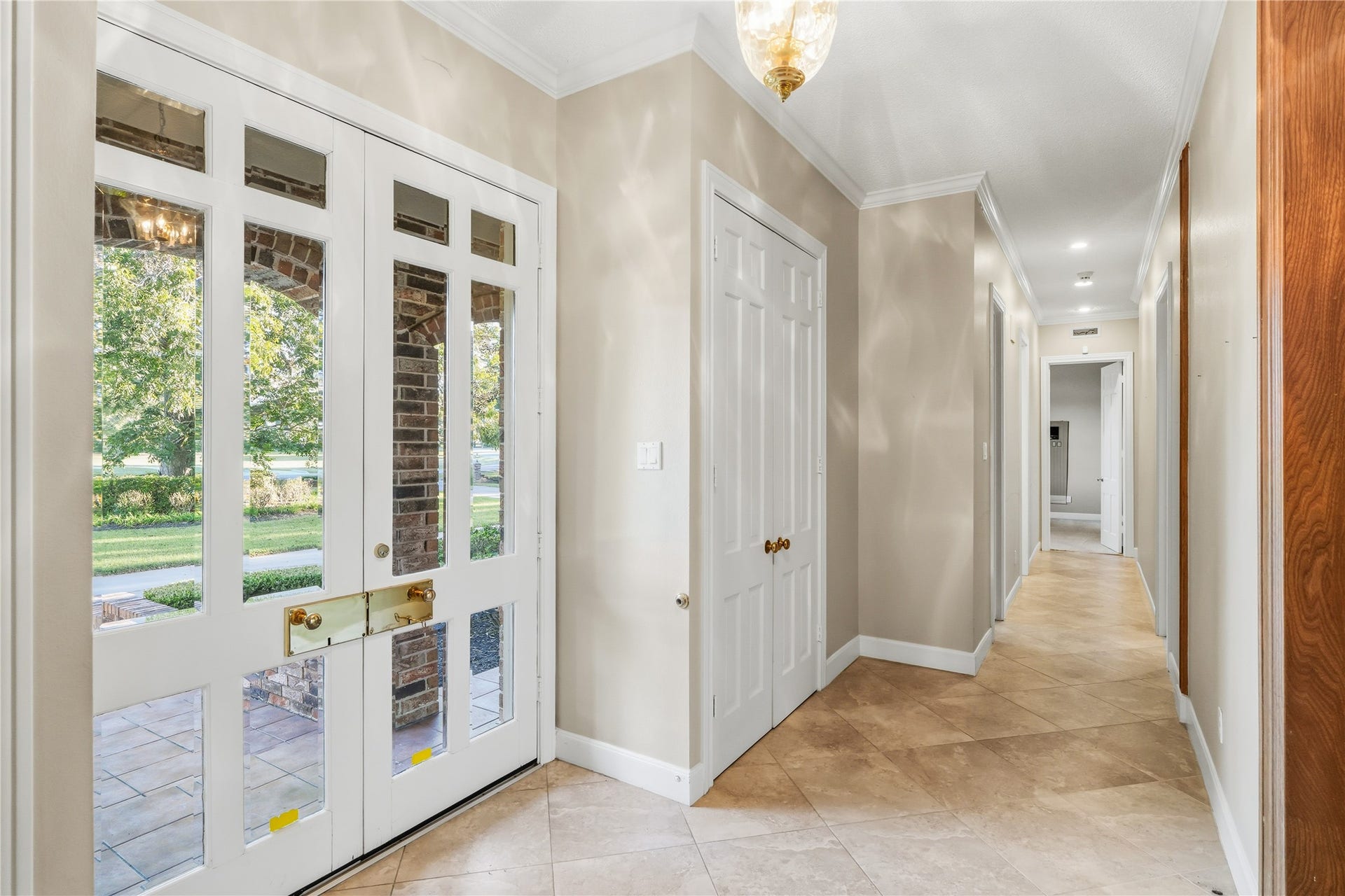 218 Bella Vista Drive, Richmond, TX 77406 Elegant entryway featuring a glass-paneled front door that opens to a bright, tiled hallway with classic crown molding and a hanging light fixture.
