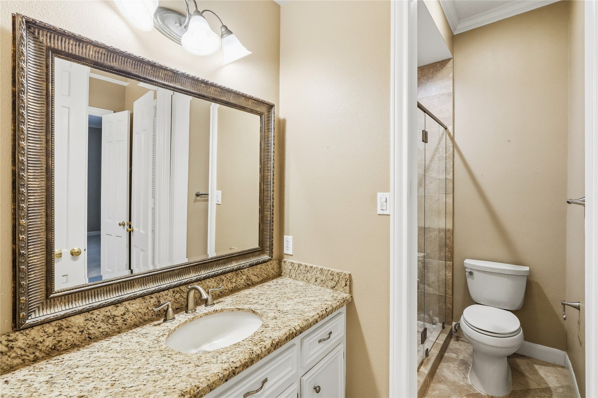 218 Bella Vista Drive, Richmond, TX 77406 Bathroom featuring a granite countertop, a large framed mirror, and a glass-enclosed shower, offering both style and functionality.