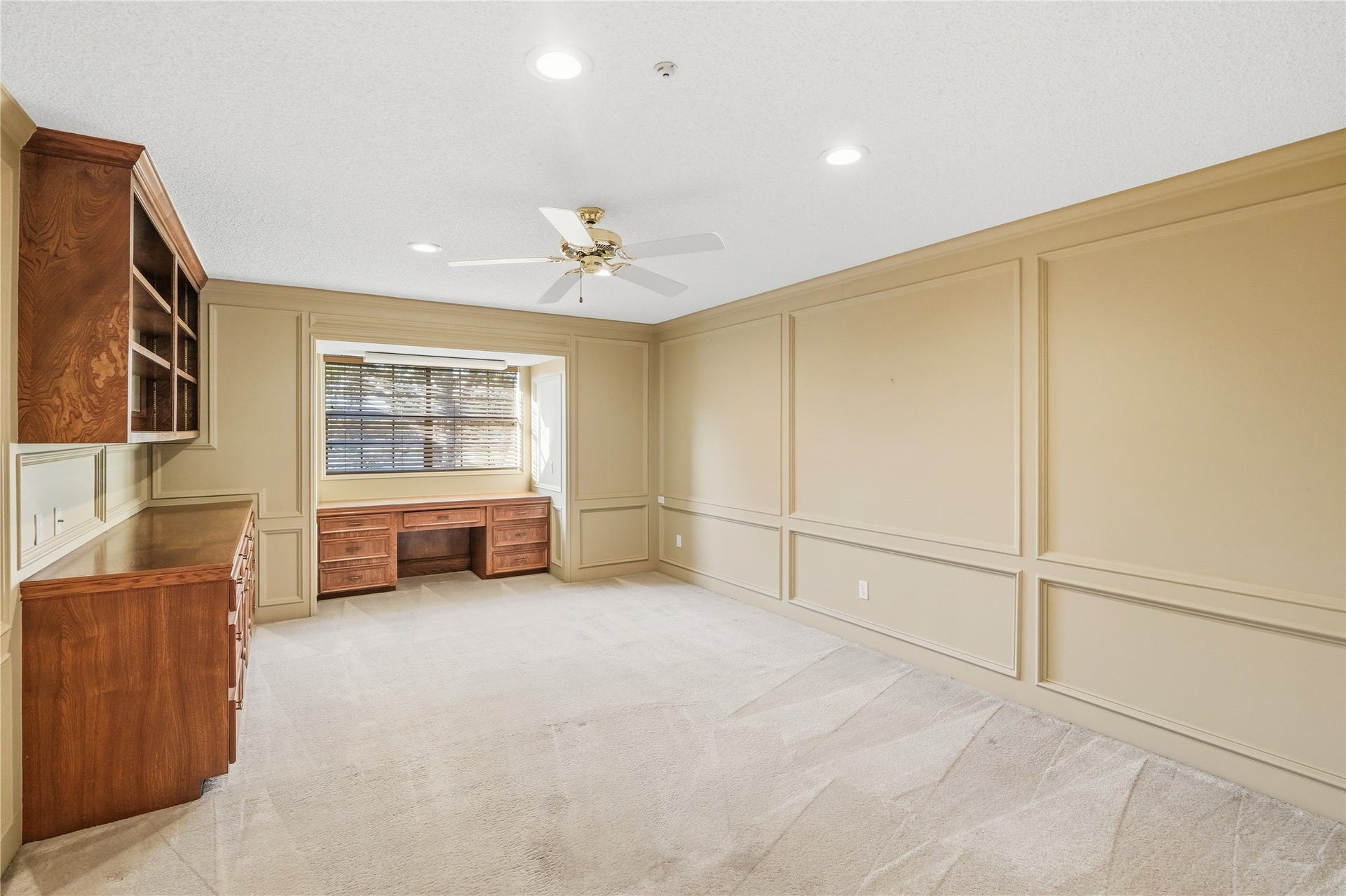 218 Bella Vista Drive, Richmond, TX 77406 Guest room with wood paneling features built-in shelving and a desk. Natural light streams through a large window, complemented by recessed lighting and a ceiling fan for comfort.
