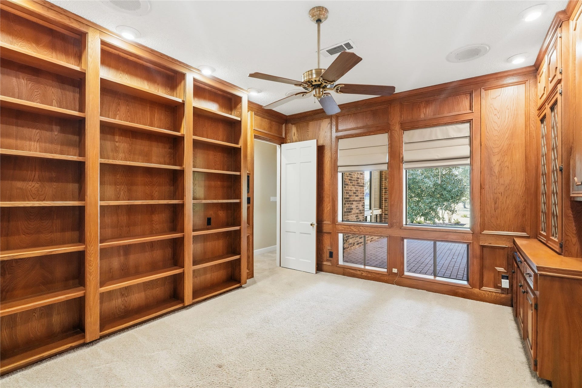 218 Bella Vista Drive, Richmond, TX 77406 Home office featuring custom built-in wooden bookshelves, a ceiling fan, and large windows with views of the backyard, creating a warm and inviting workspace.