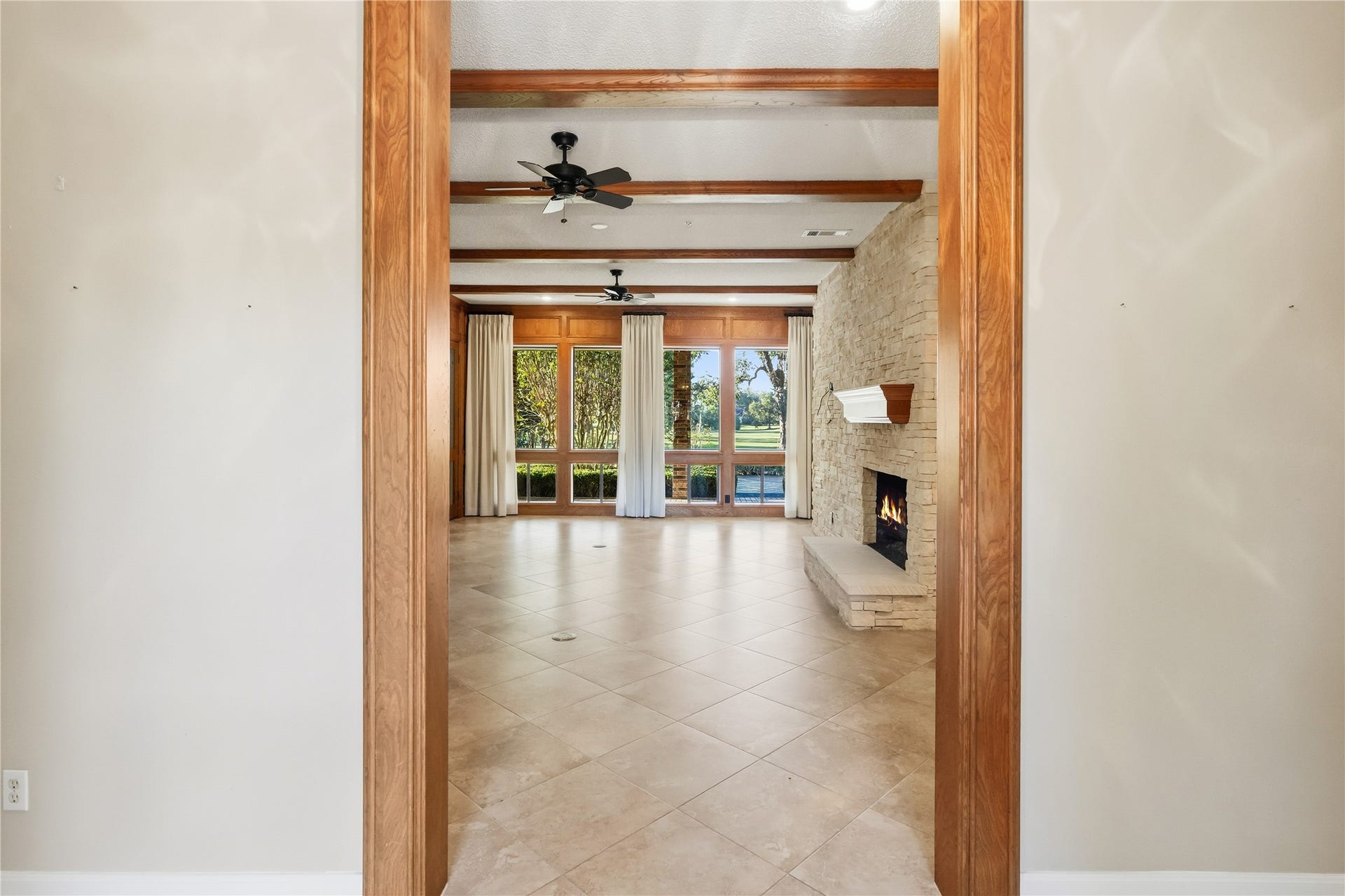 218 Bella Vista Drive, Richmond, TX 77406 Elegant living room with a cozy stone fireplace, large windows offering scenic views, and rich wood beam accents on the ceiling.