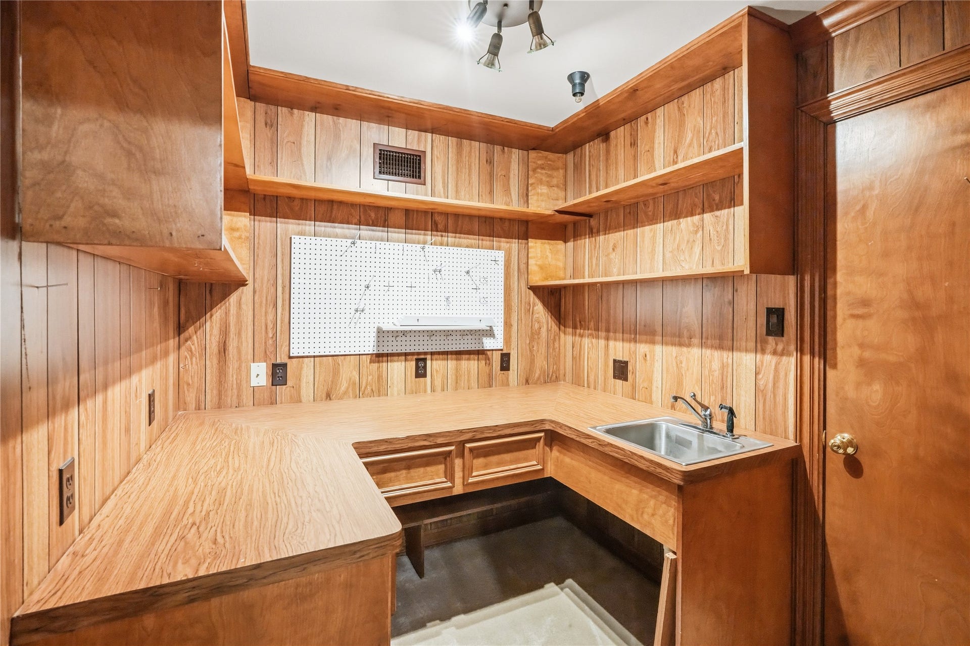 218 Bella Vista Drive, Richmond, TX 77406 Cozy workshop space with warm wood paneling, ample shelving for storage, and a convenient utility sink for versatile use.