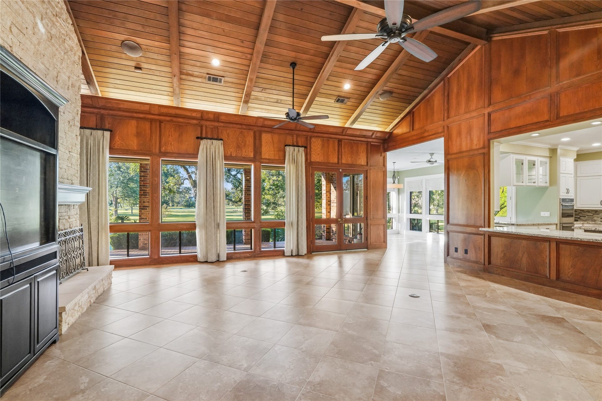 218 Bella Vista Drive, Richmond, TX 77406 Spacious living area with vaulted wood ceilings, large windows offering stunning views, and a cozy stone fireplace, seamlessly connected to the bright kitchen.