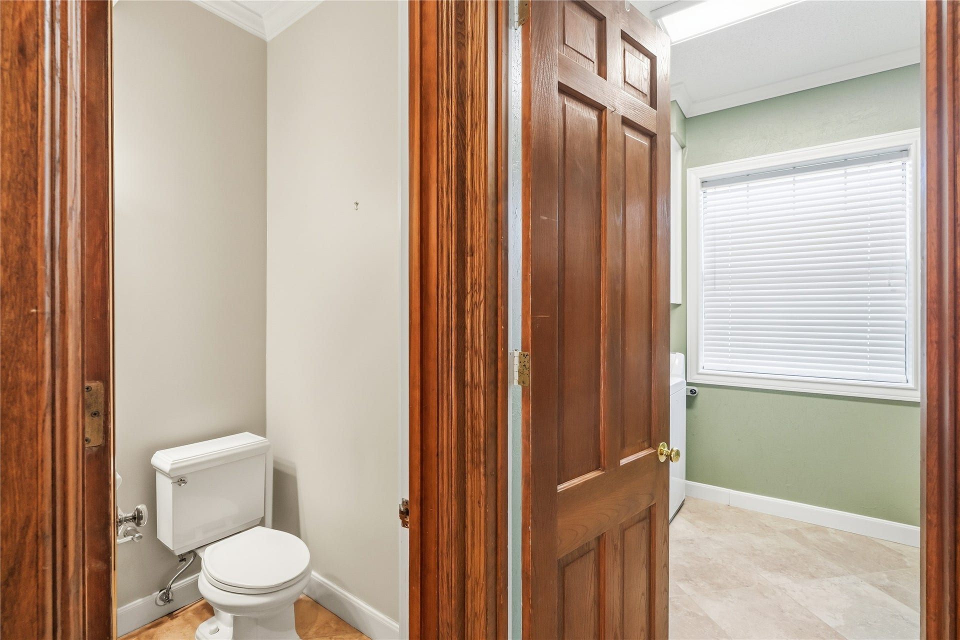 218 Bella Vista Drive, Richmond, TX 77406 Powder room with elegant wooden door, adjacent to a bright laundry room featuring a window with blinds, offering privacy and natural light.