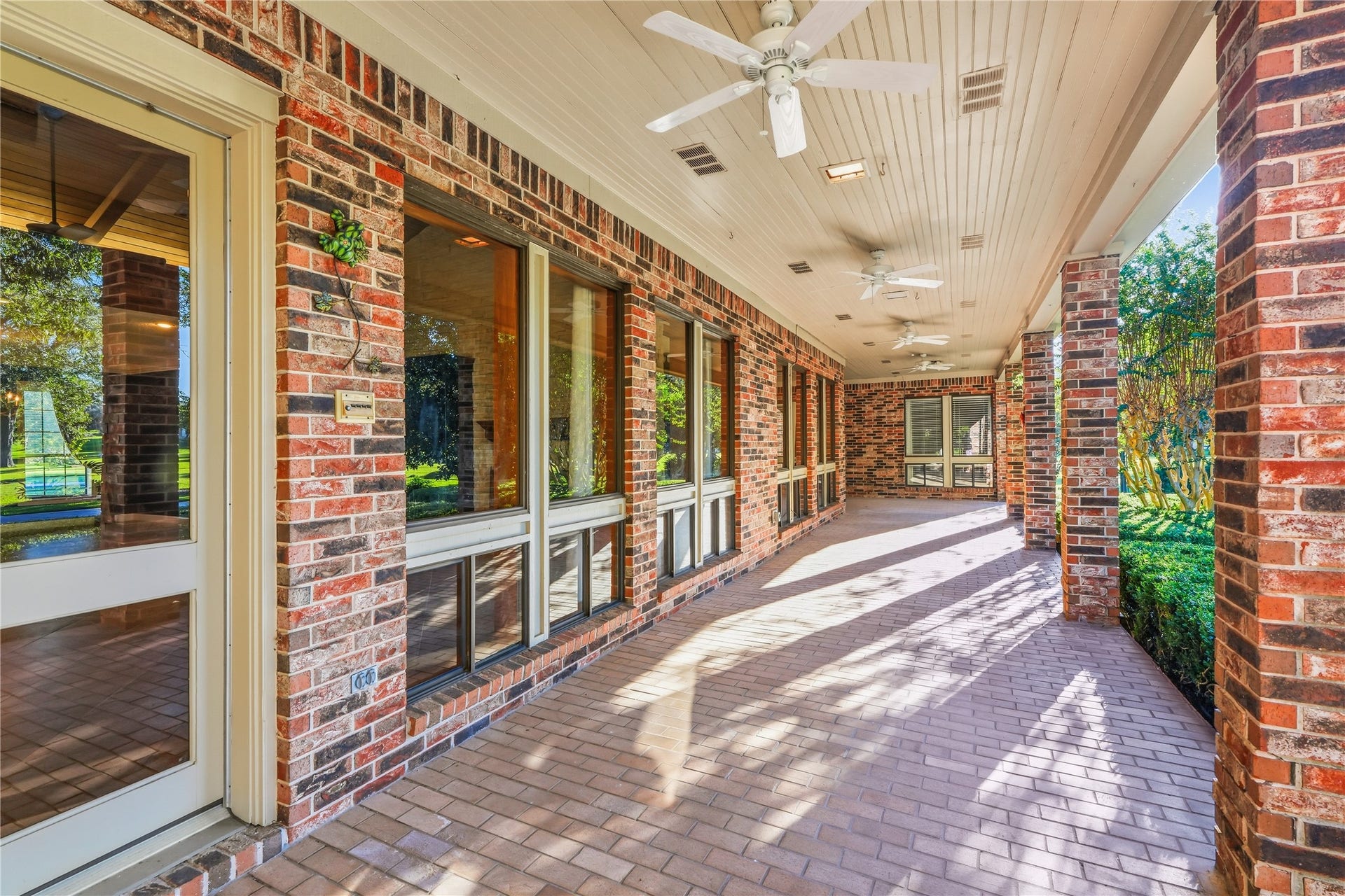 218 Bella Vista Drive, Richmond, TX 77406 The covered patio off the back of the house with charming brickwork, ceiling fans, and large windows offering serene views of the surrounding yard space .