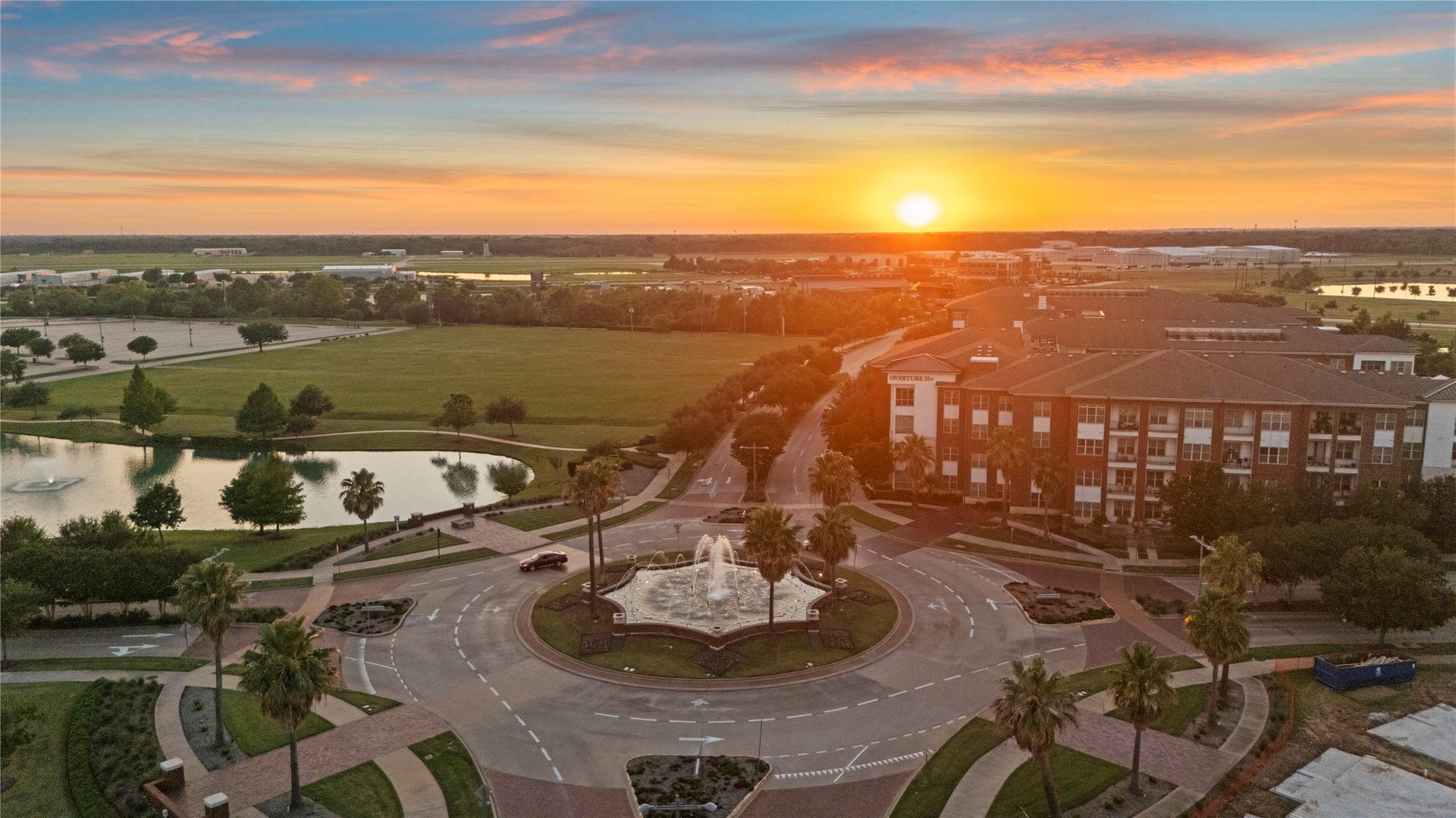 11 Victorian Run, Sugar Land, TX 77498 Golden hour spills across a palm-lined roundabout, where glowing fountains, quiet lakes, and elegant streets create a dreamy suburban sunset scene.