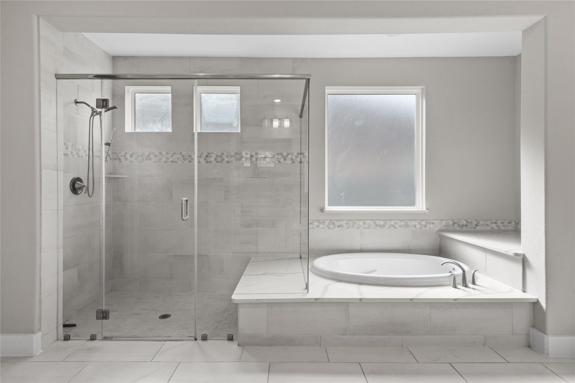 11 Victorian Run, Sugar Land, TX 77498 Luxurious primary bath featuring a walk-in glass shower with tile surround and decorative accent band, alongside a relaxing soaking tub. The well-designed layout offers a spa-like feel with natural light and elegant finishes throughout.