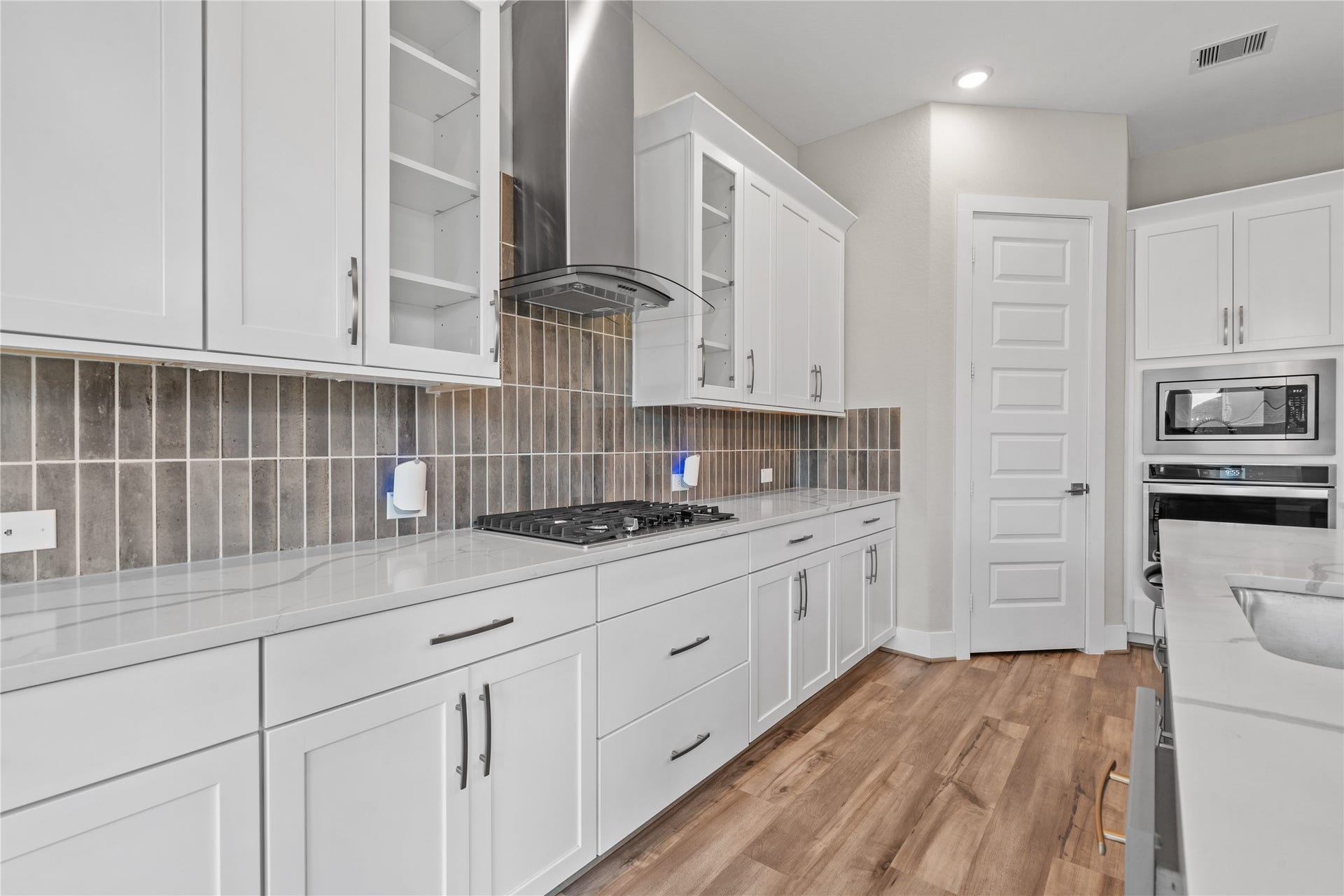 11 Victorian Run, Sugar Land, TX 77498 Modern kitchen workspace featuring a gas cooktop, sleek vent hood, and extended quartz countertops for ample prep area. The combination of stylish cabinetry and detailed backsplash adds both functionality and visual appeal.