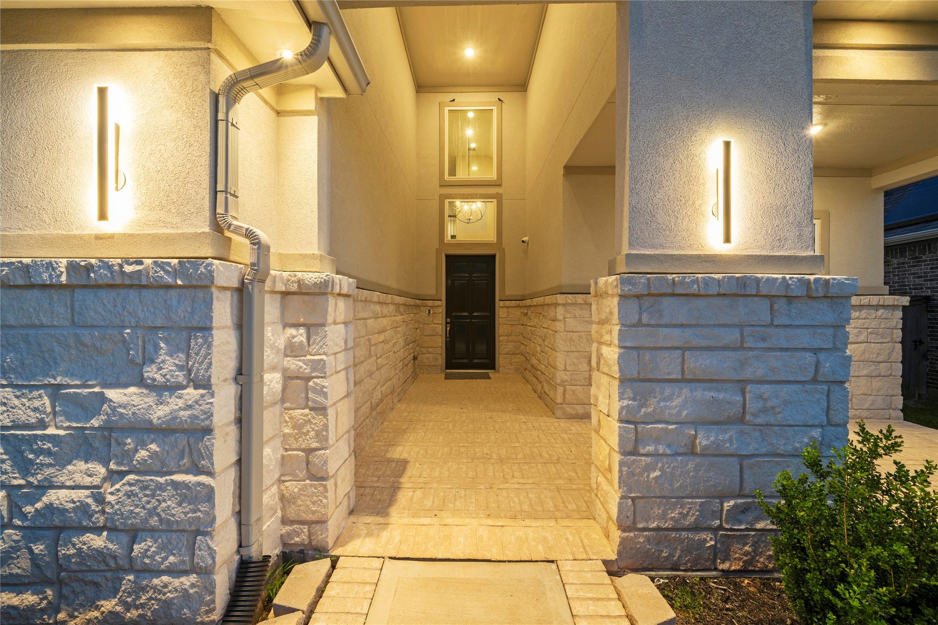 11 Victorian Run, Sugar Land, TX 77498 A grand modern entryway glows with warm ambient lighting, framed by textured stone columns and clean architectural linescreating a luxurious, welcoming first impression.